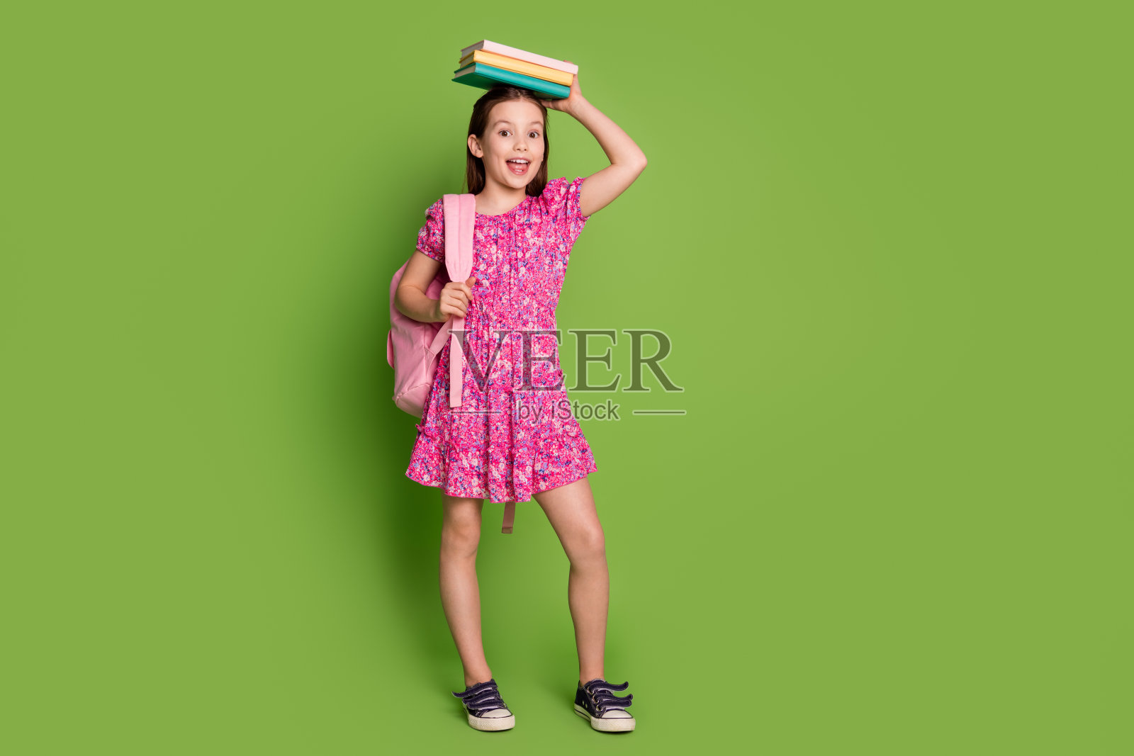 可爱的女学生的全尺寸照片，抱着书头，穿着粉红色的衣服，孤立在绿色的背景上照片摄影图片
