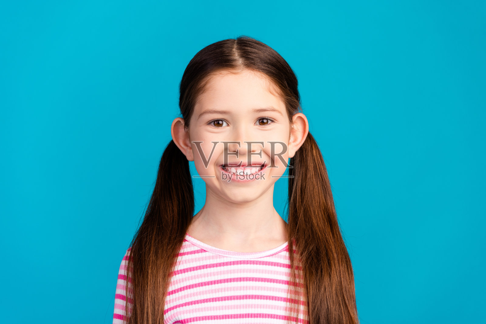 可爱的积极乐观的小女孩，扎着马尾辫，穿着条纹衬衫，牙齿微笑，孤立在蓝色背景下照片摄影图片