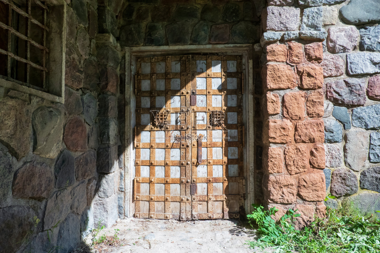 这座带有沉箱墙的古老哥特式建筑的入口大门用金属带加固。有带栏杆的窗户。背景。照片摄影图片