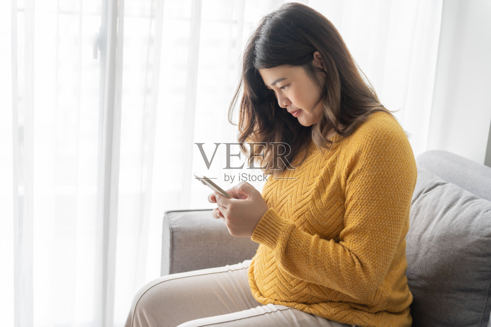 亚洲孕妇在家拿着智能手机，使用孕妇手机应用照片摄影图片