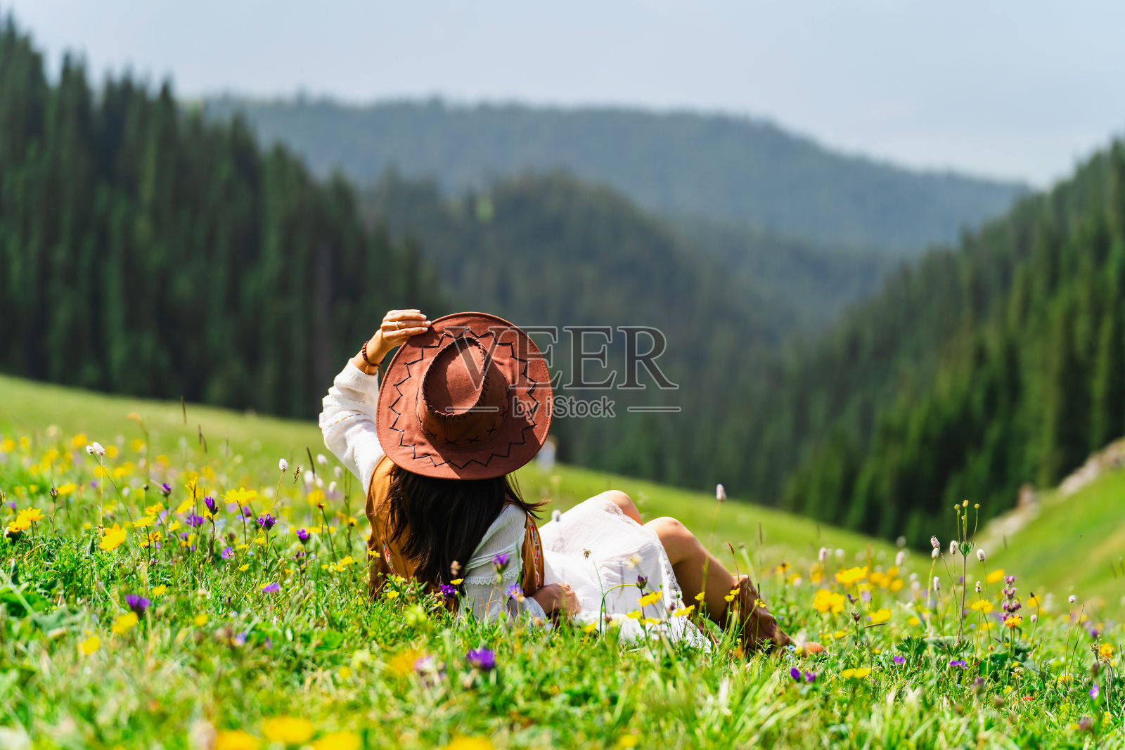 夏天，年轻的女游客在新疆喀拉君草原上放松身心，欣赏着美丽的风景和五彩缤纷的花朵照片摄影图片