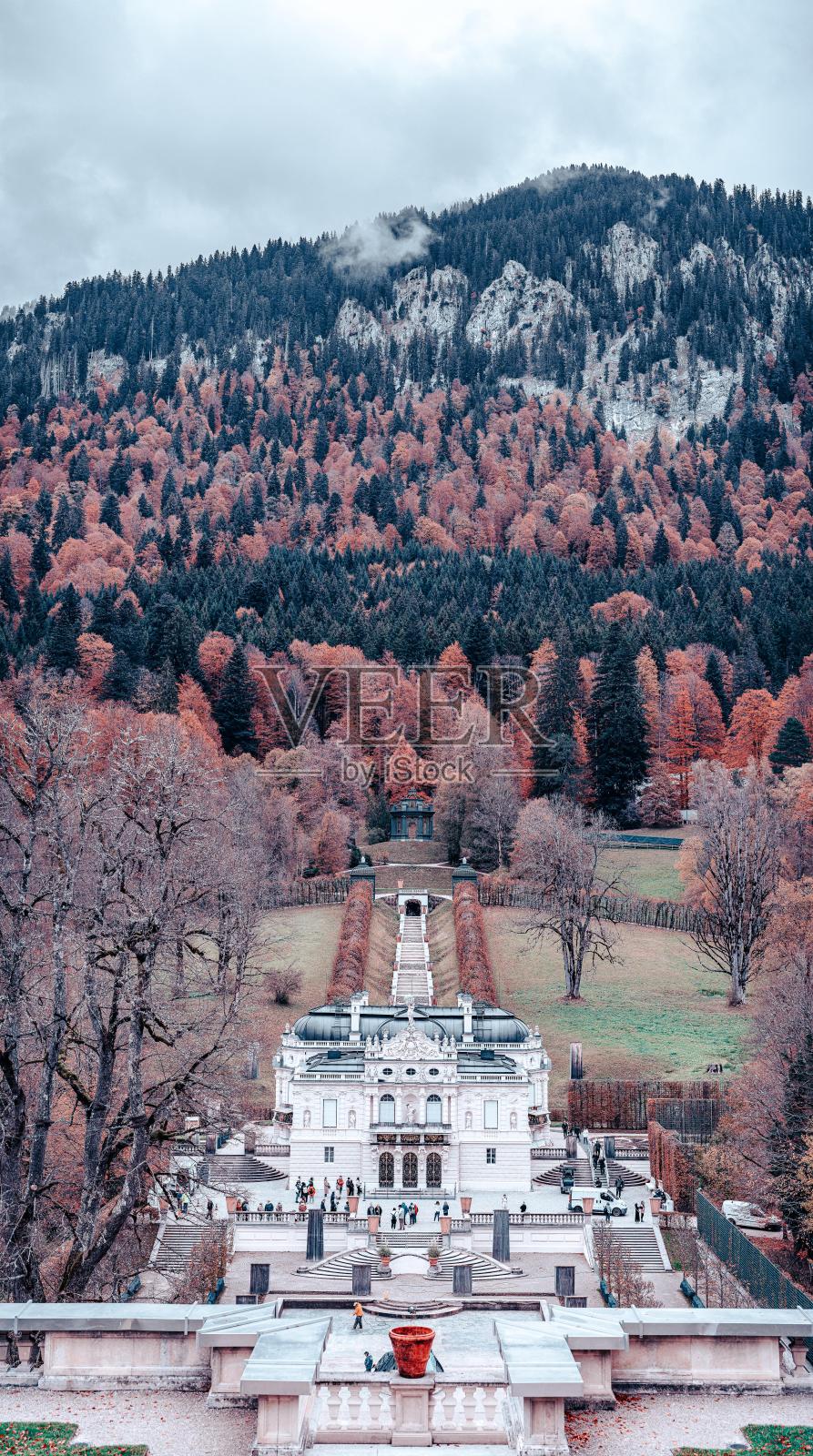 一座白色外墙的宫殿坐落在群山背景的山谷中。一条走道通向入口,人们在周围散步。照片摄影图片