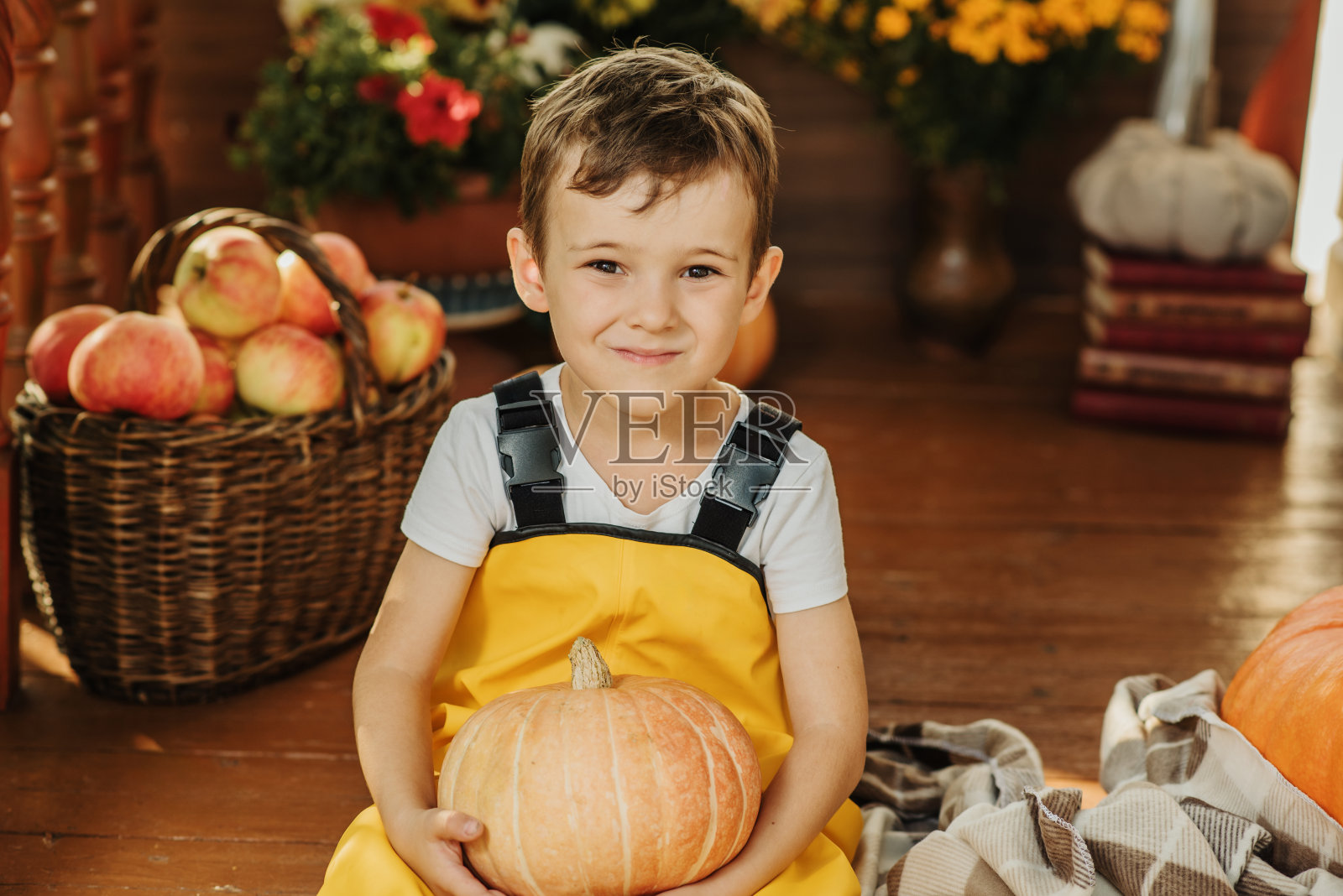 一个穿着黄色连体衣的白人男孩的肖像，坐在秋天用南瓜装饰的门廊上。照片摄影图片