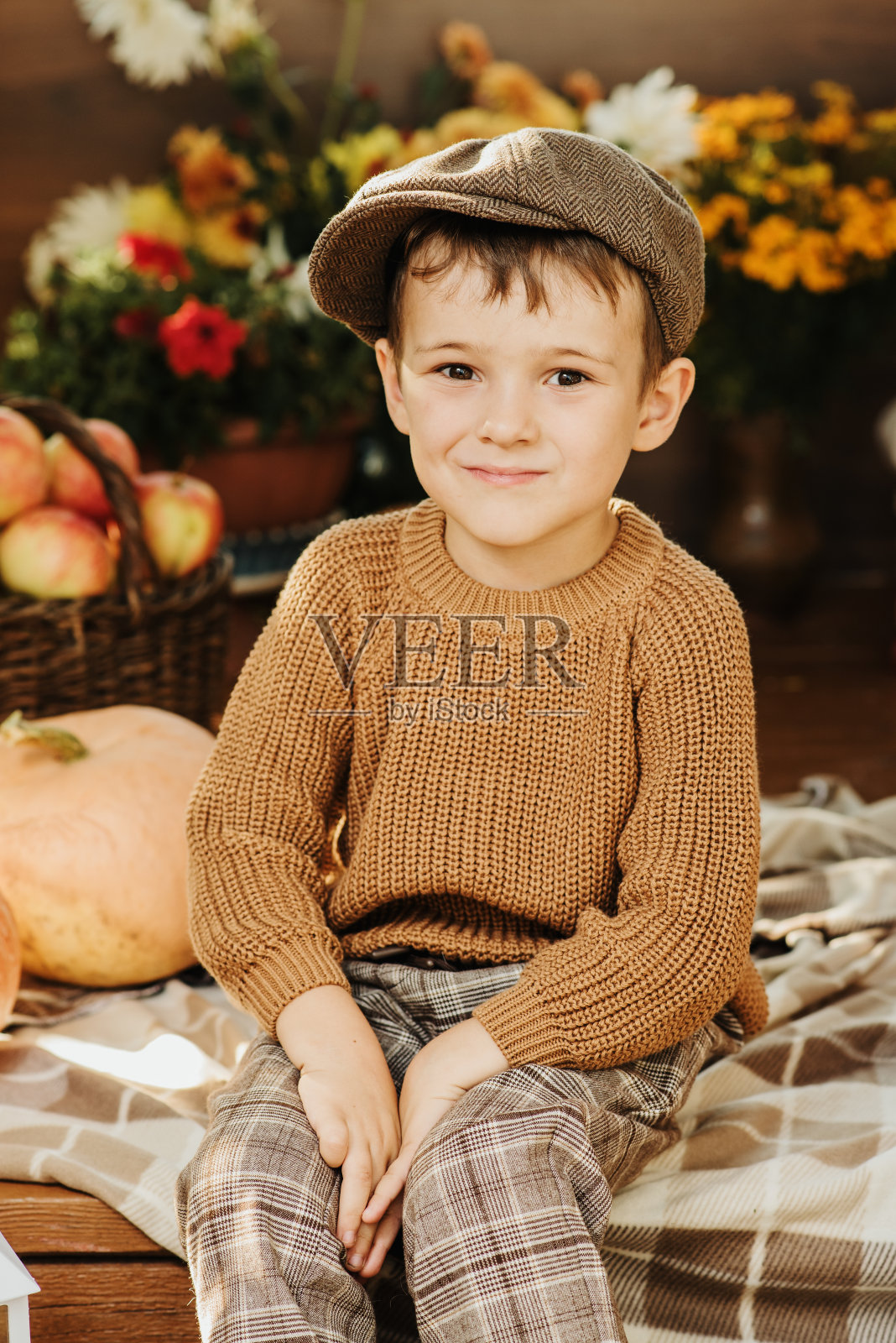 秋天，一个穿着毛衣的白人男孩坐在用南瓜装饰的门廊上。照片摄影图片