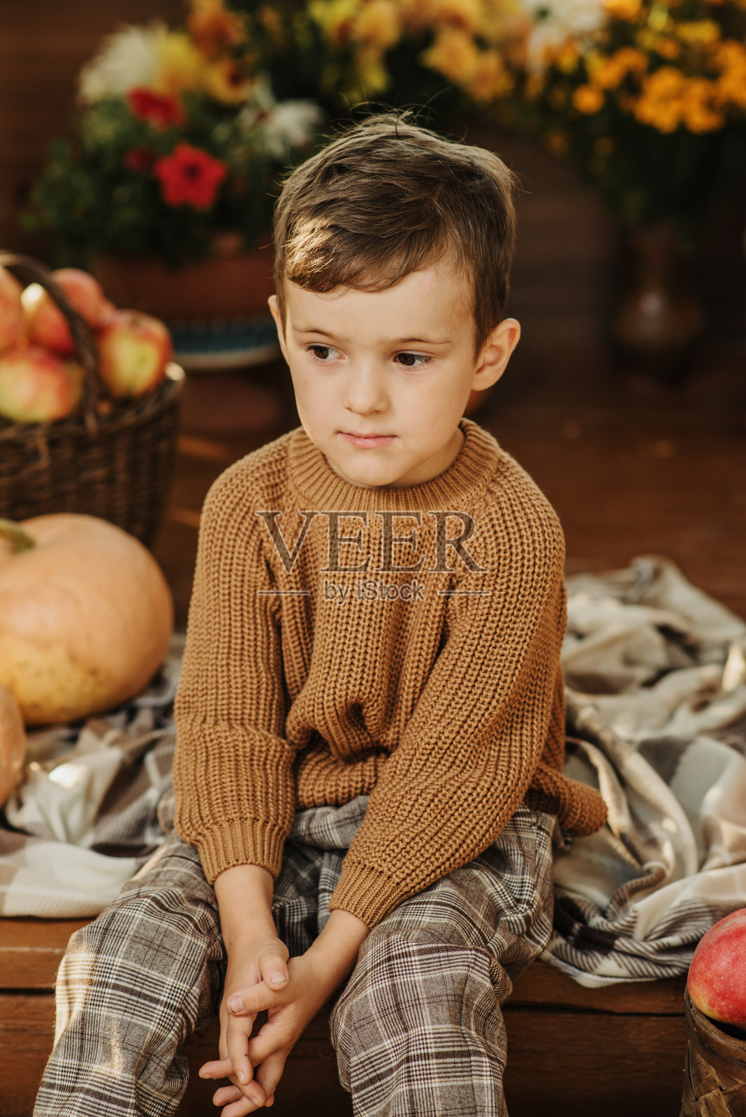 秋天，一个穿着毛衣的白人男孩坐在用南瓜装饰的门廊上。照片摄影图片