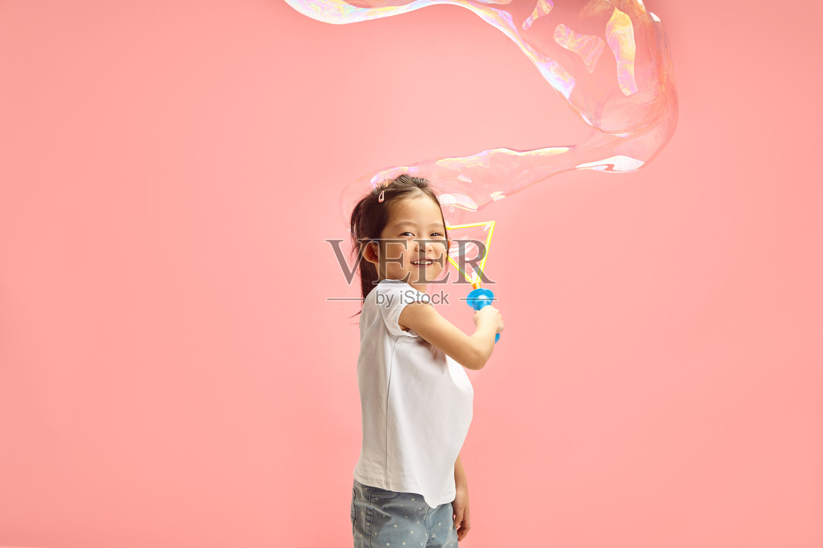 可爱和快乐的小女孩吹大肥皂泡周围自己站在粉红色孤立的背景照片摄影图片