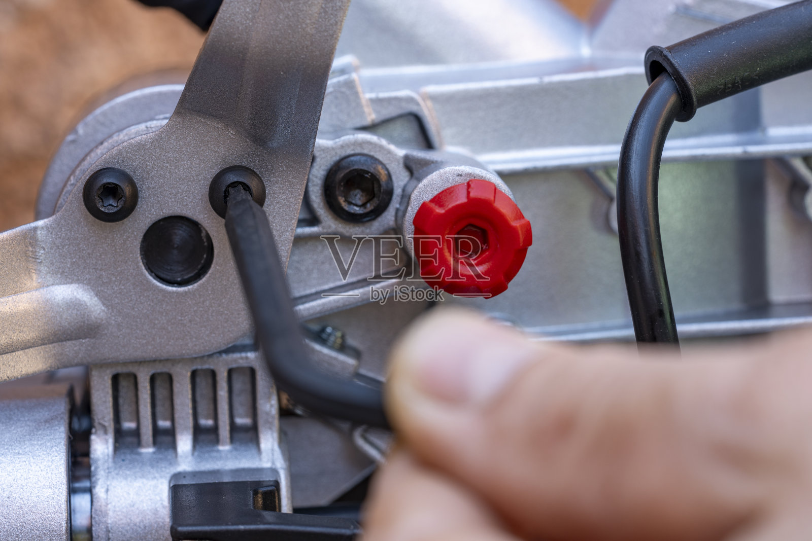 一名男子用六角扳手拧下螺栓，用于调节人字锯(特写)。工人用扳手操作内六角螺丝照片摄影图片