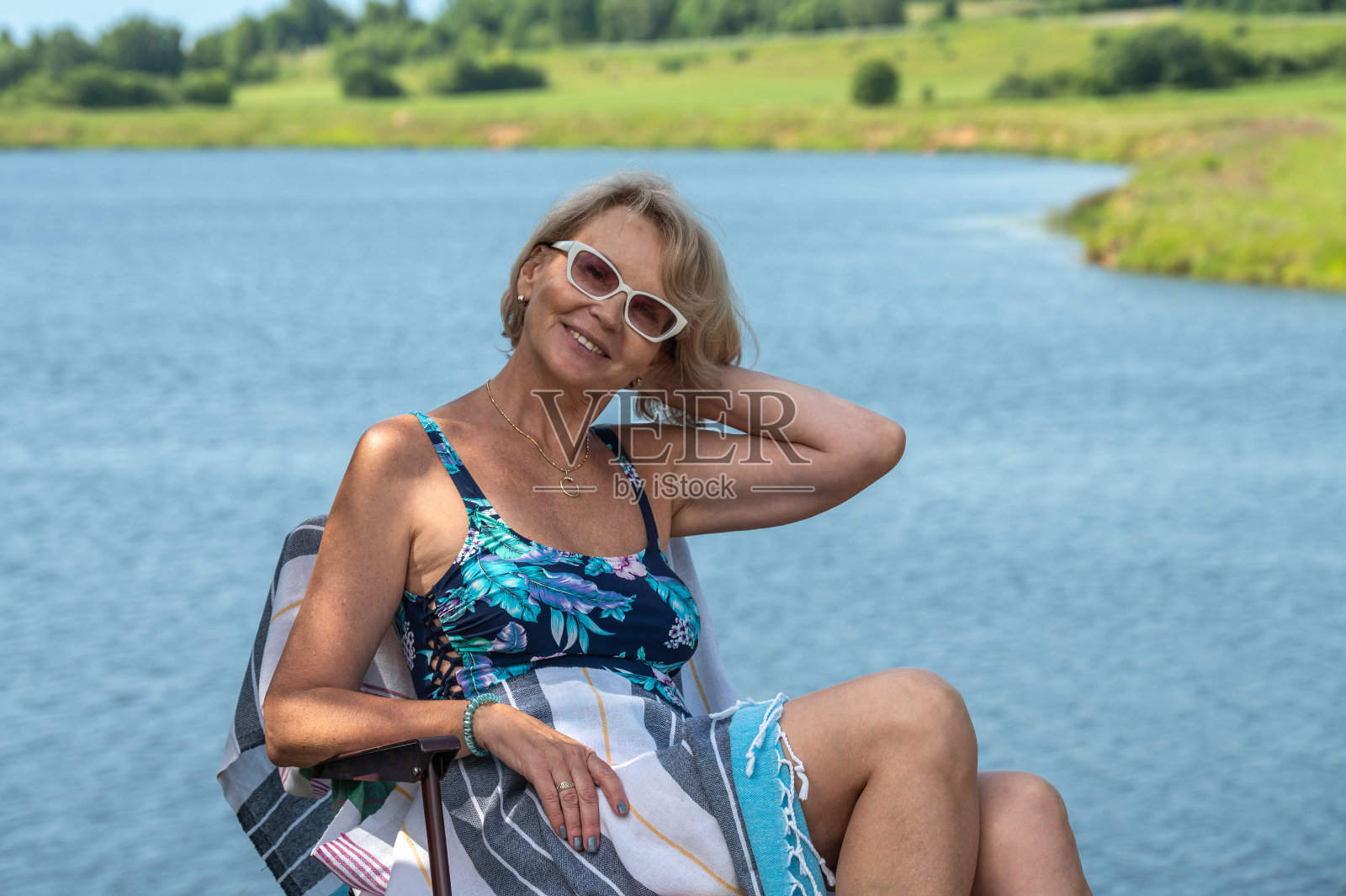 一个穿着泳装的成熟的女人坐在河岸的躺椅上。照片摄影图片