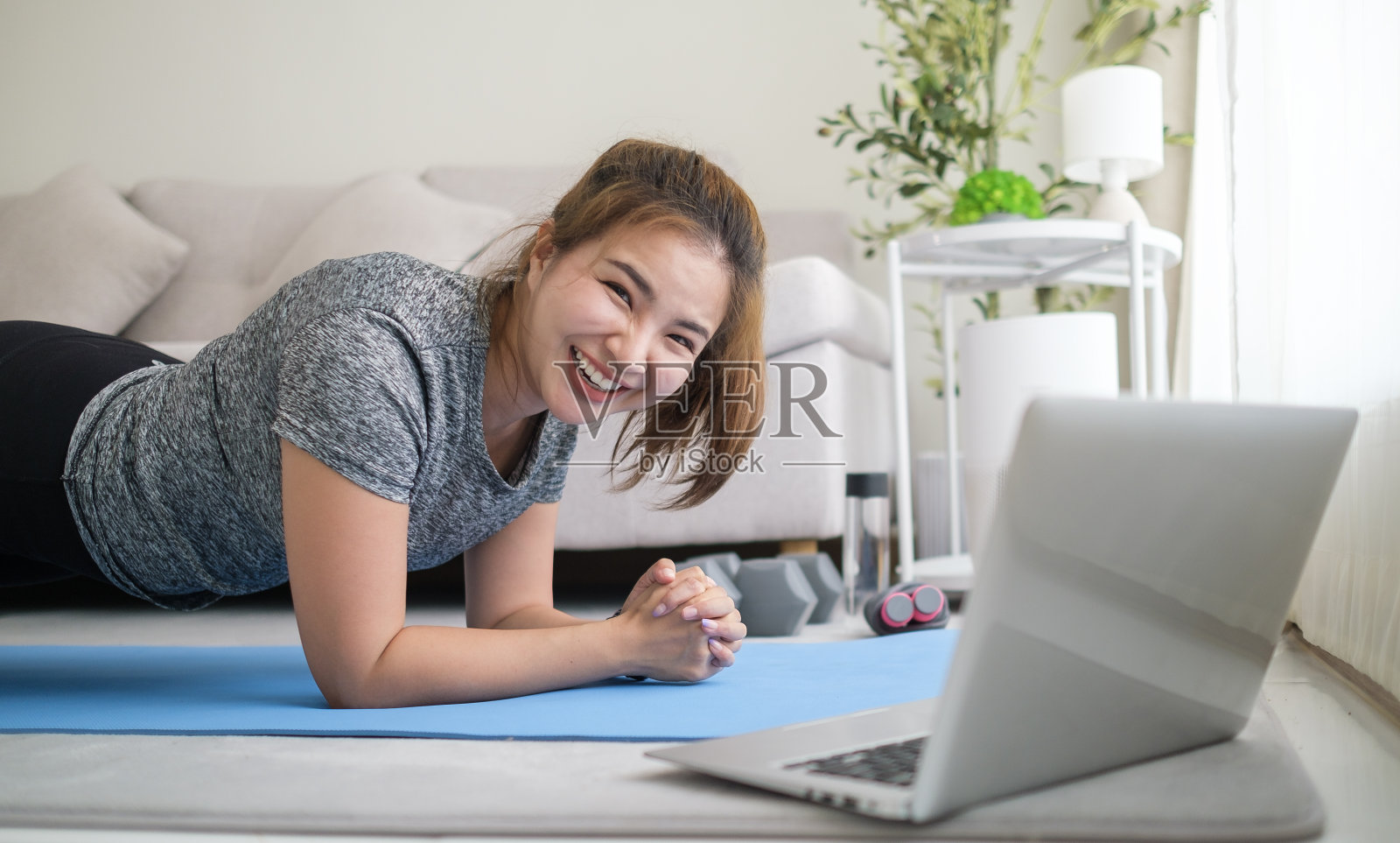 漂亮的年轻女子一边在客厅的笔记本电脑上看在线教程，一边做瑜伽平板支撑。照片摄影图片
