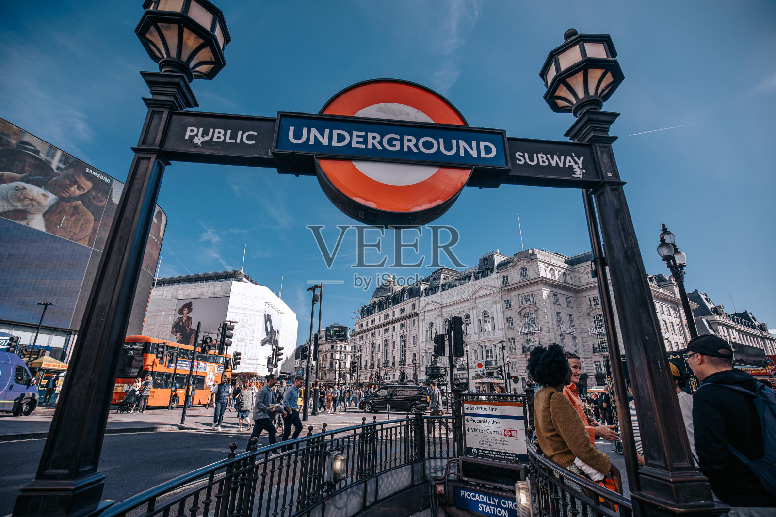 摄政街的伦敦地铁站入口，有红色的圆圈标志，路灯和蓝天。牌子上写着“公共地铁”，有行人经过，背景是一辆公共汽车。照片摄影图片