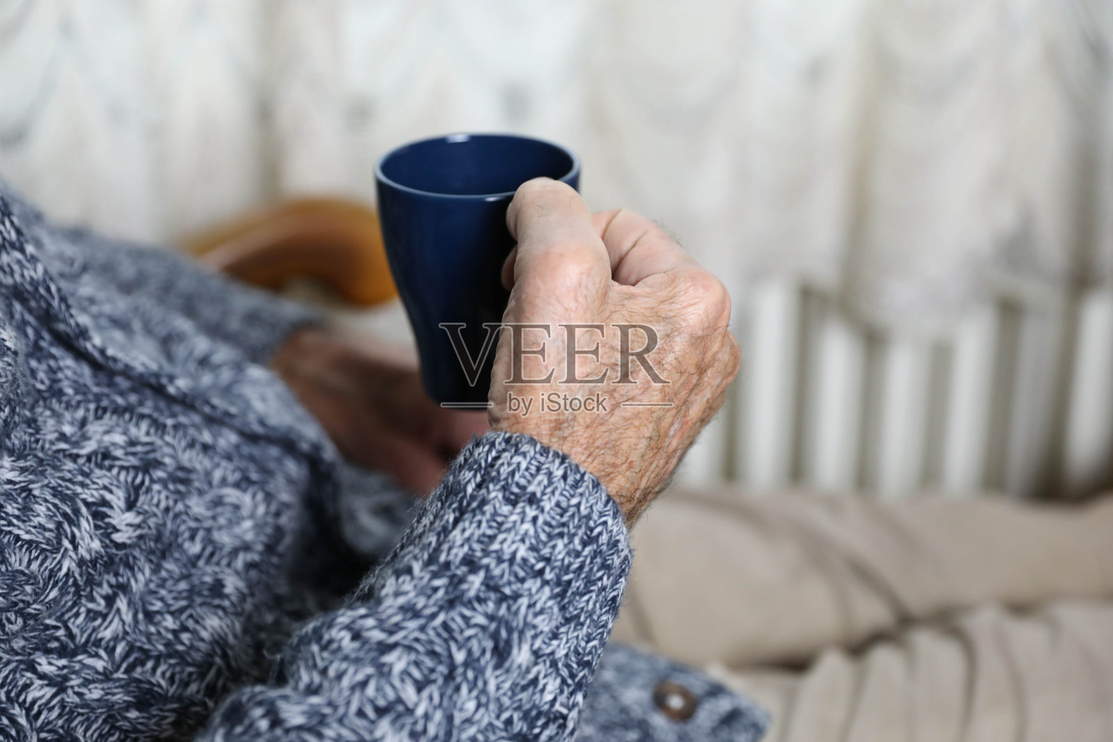 一个年长的男人坐在椅子上，穿着白衬衫和灰色毛衣，手里拿着一杯咖啡。照片摄影图片