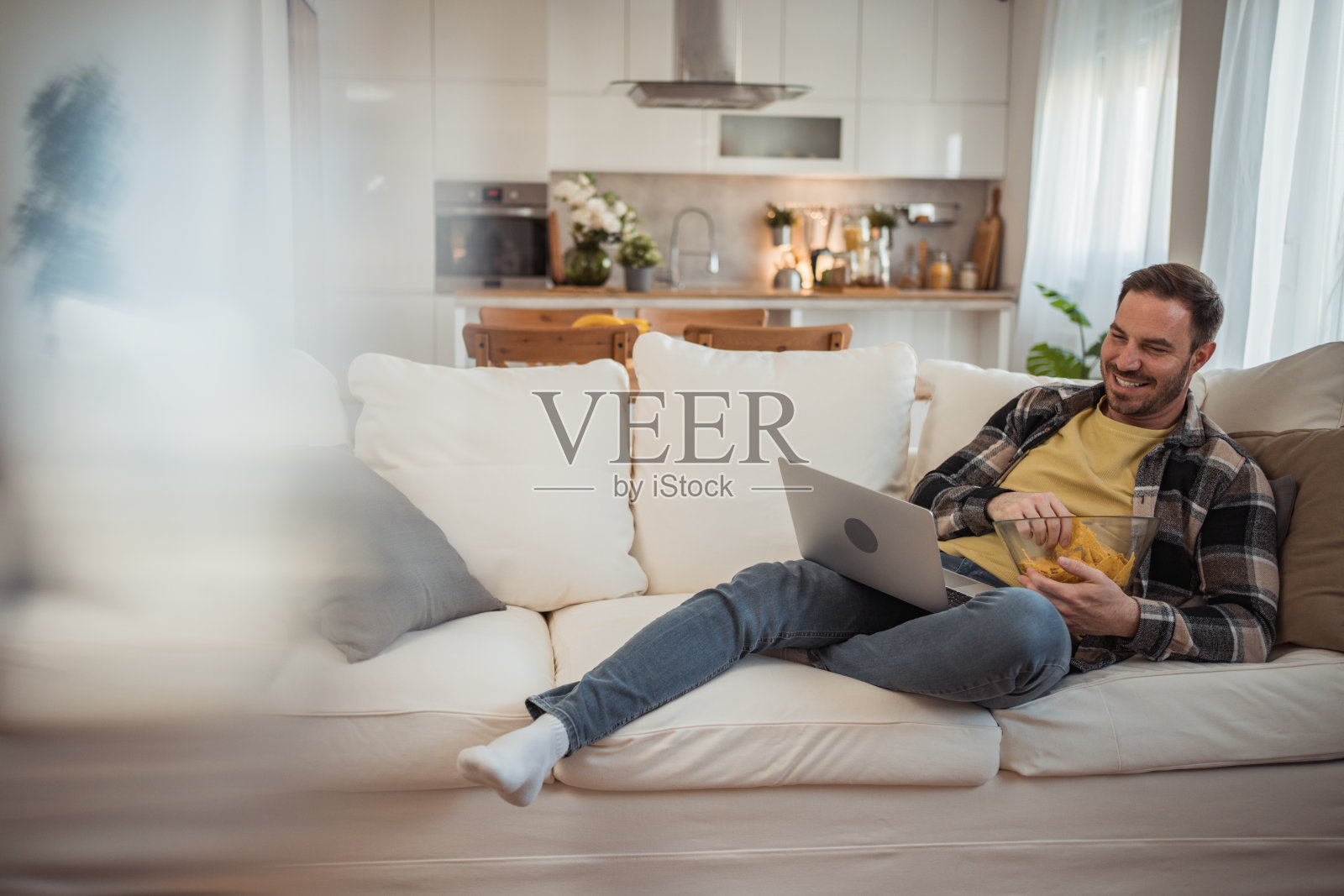 一个年轻人坐在客厅的沙发上，用新的流媒体中心观看电影，专注地盯着笔记本电脑的屏幕照片摄影图片