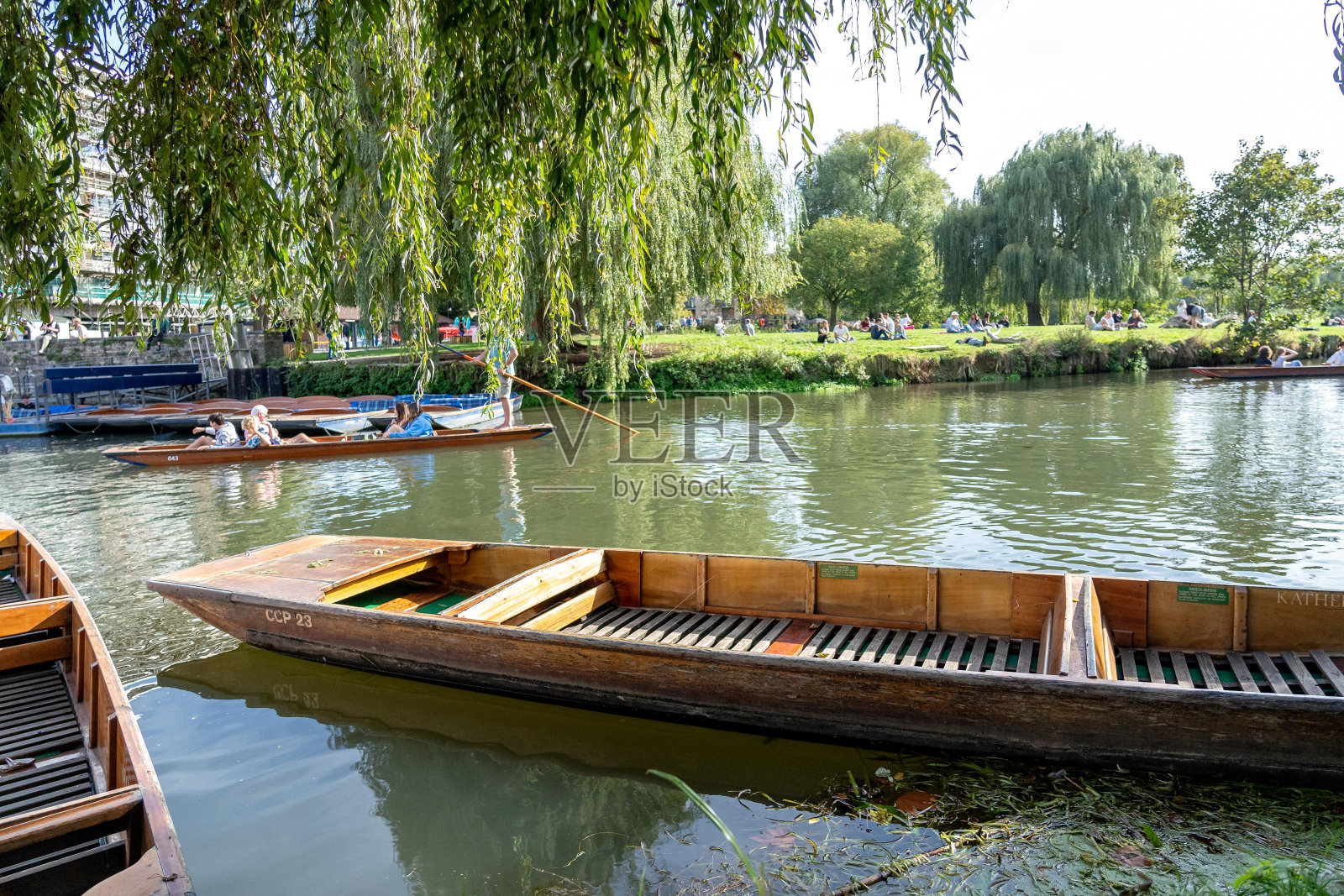 英国剑桥康河上的一艘木船,背景是郁郁葱葱的绿叶。水面平静,映着蓝天。照片摄影图片