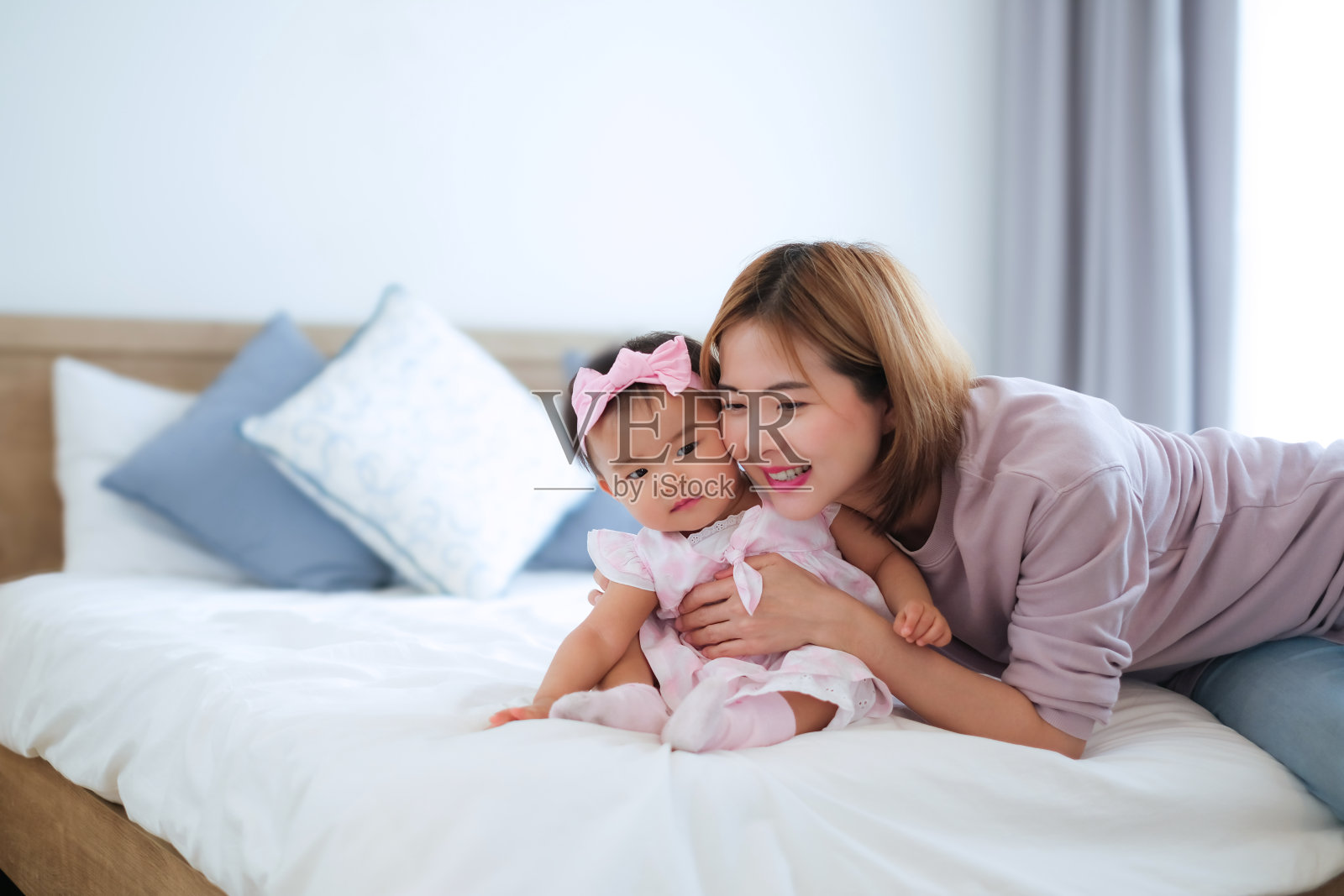 小女孩坐在床上，她的妈妈拥抱着，两颊紧紧地贴在一起。儿童肖像和医疗保健概念。照片摄影图片