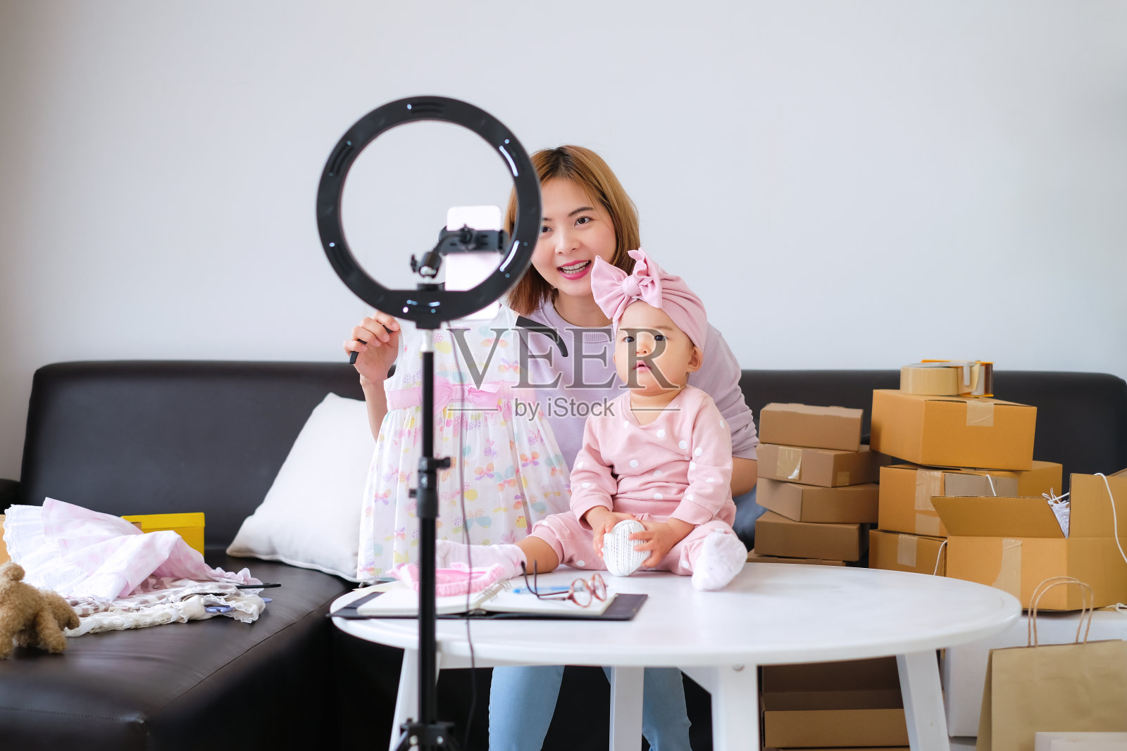 可爱的小女孩和她的亚洲妈妈，时尚和美容博主展示了孩子们的裙子，让在线客户在直播时观看。照片摄影图片