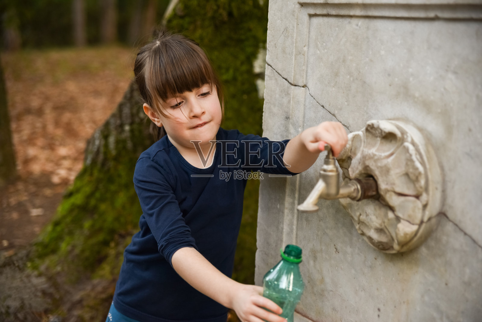 女孩从公园的喷泉里把水倒进瓶子里照片摄影图片