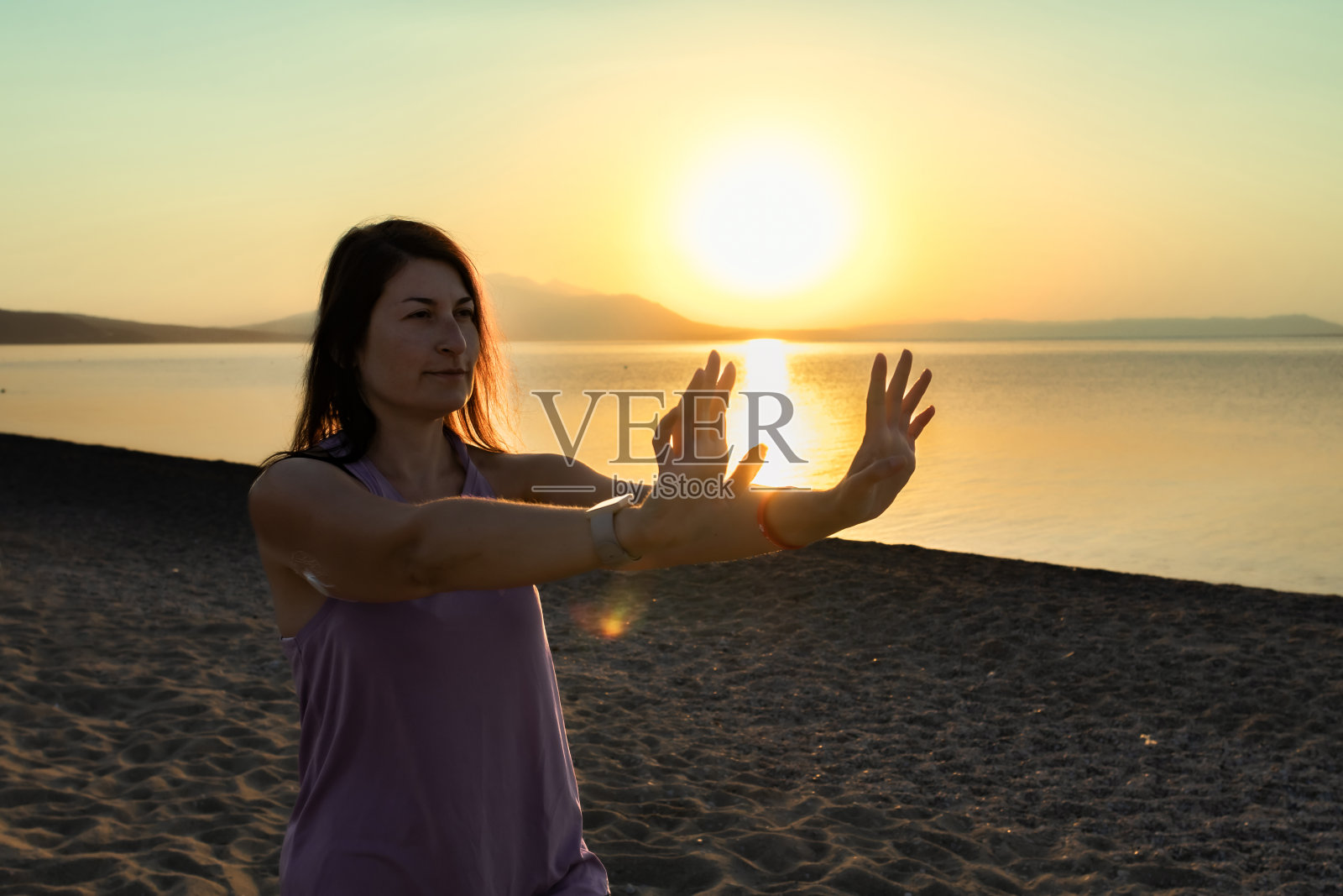 中年糖尿病妇女在日落或日出时在海边的沙滩上练习太极。轮廓。健康、积极的生活方式。运动与糖尿病。一位女士在上臂背部佩戴了控制血糖的小传感器。照片摄影图片