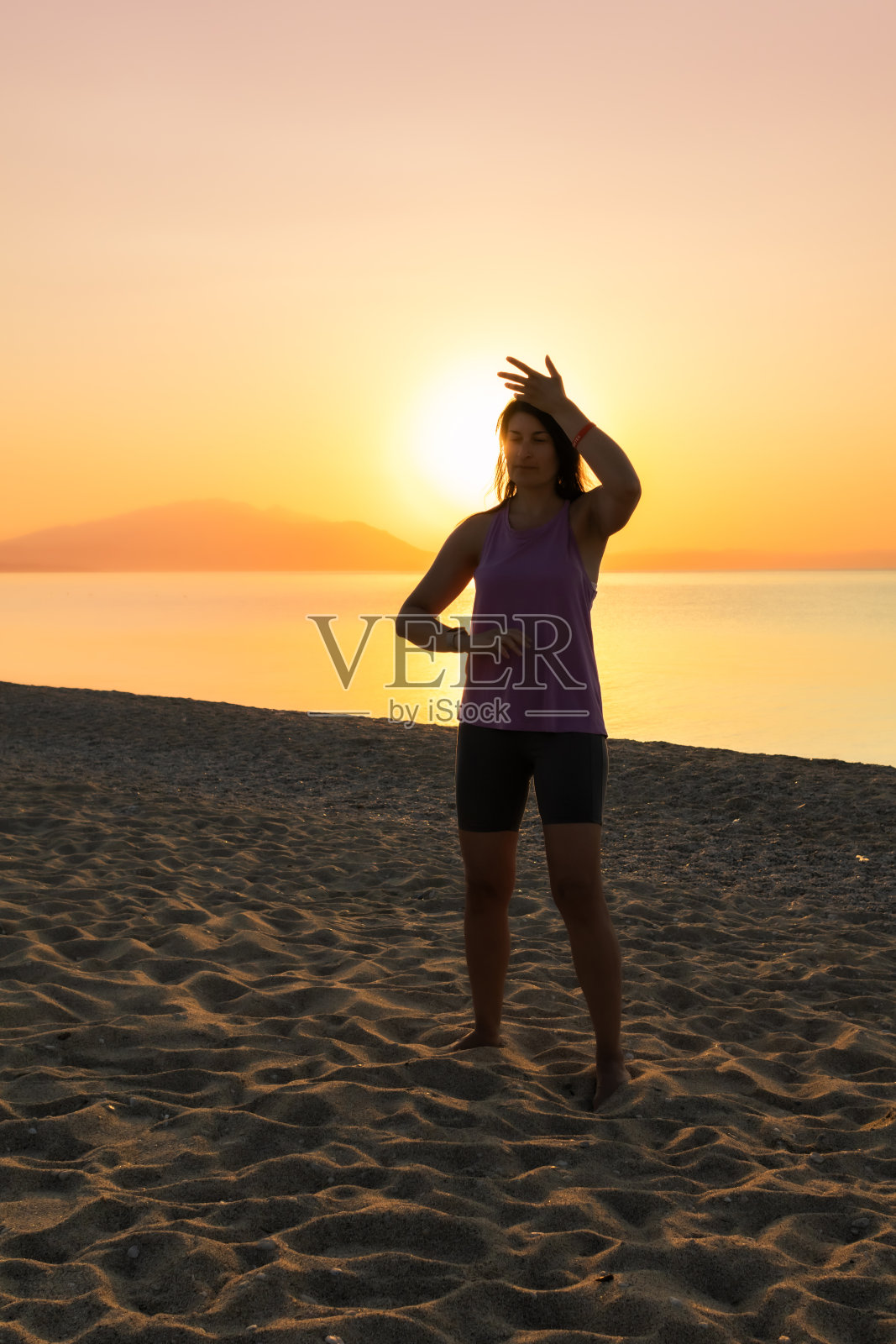 中年成年妇女在日落或日出时在海边的海滩上练习太极。夕阳下打太极的剪影。健康、积极的生活方式。照片摄影图片