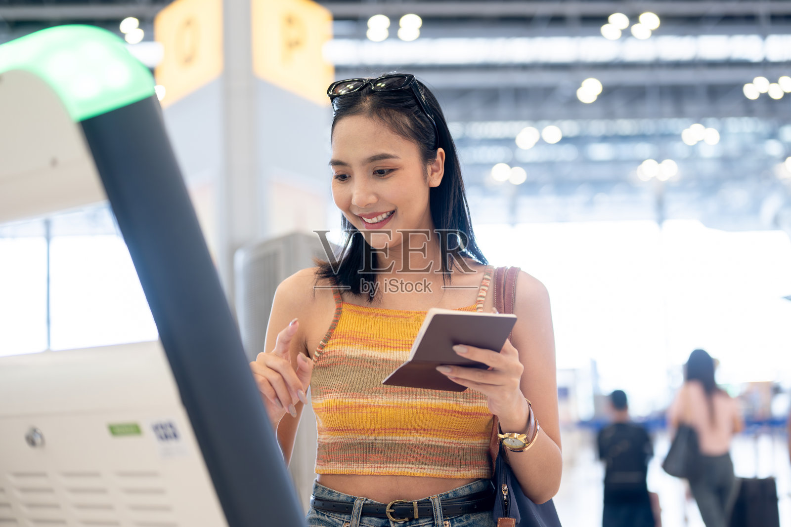 一位美丽的亚洲女乘客正在机场航站楼使用机场自助值机亭。照片摄影图片