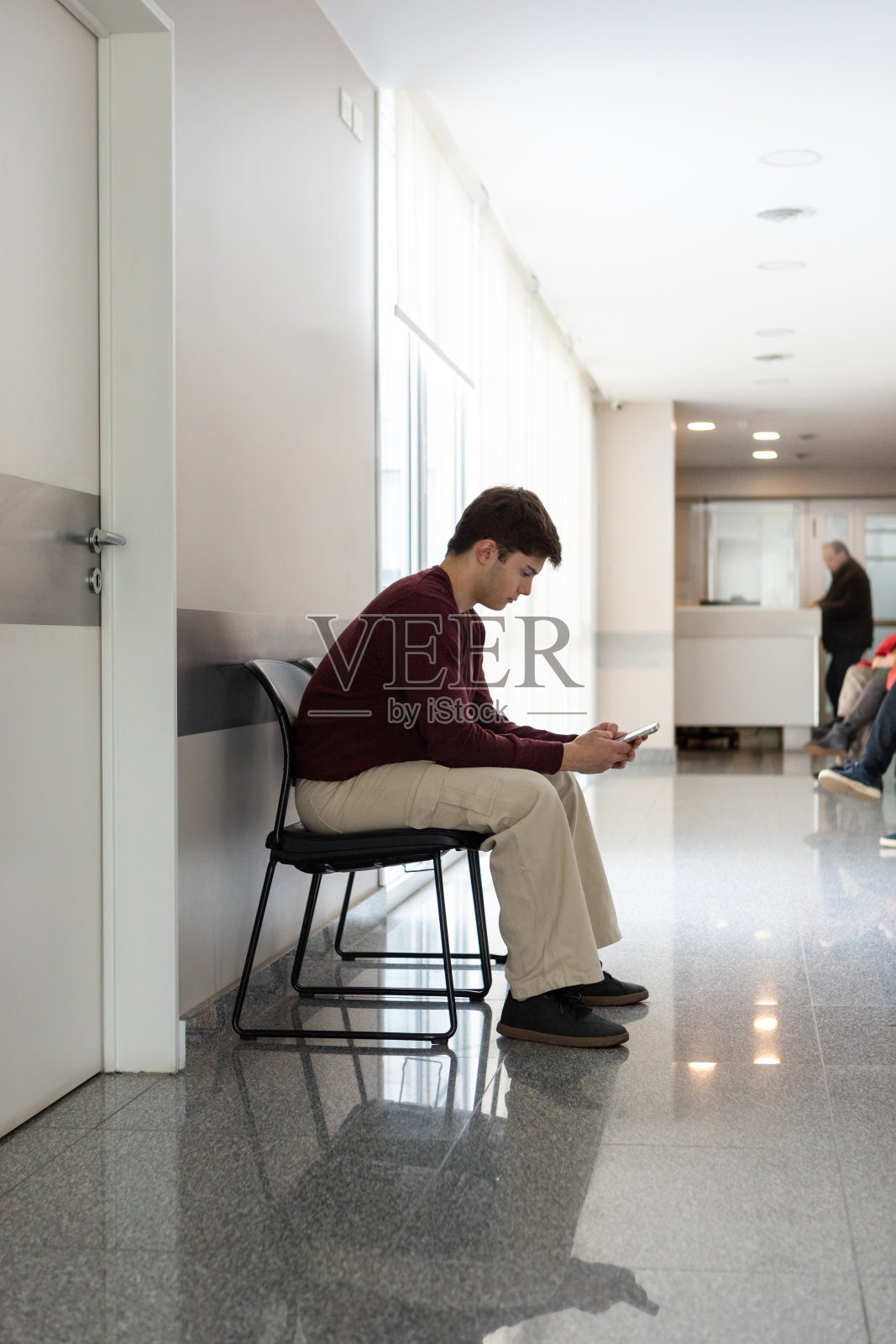 一名男性青少年在诊所候诊室使用智能手机照片摄影图片