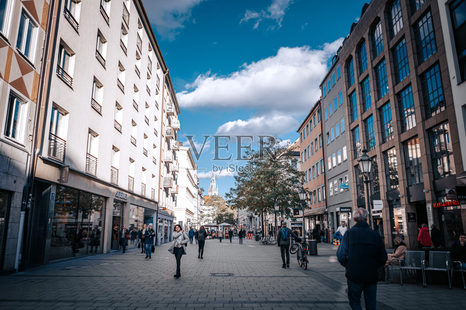 一条高楼林立的步行街，人行道上走着几个人，一个人推着自行车。照片摄影图片