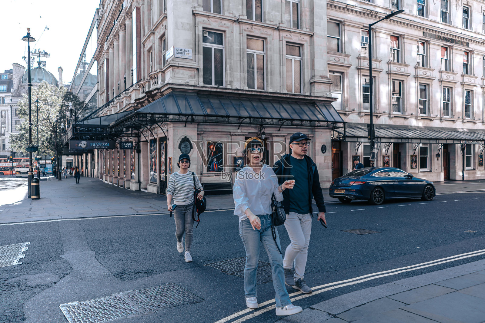 三个人走在英国伦敦摄政街附近的一条街上,背景中停着一辆汽车。照片摄影图片