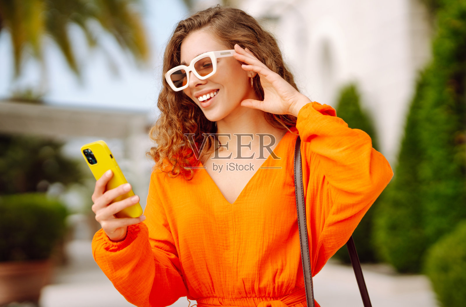 年轻女子走在街上用智能手机，与朋友交流。照片摄影图片