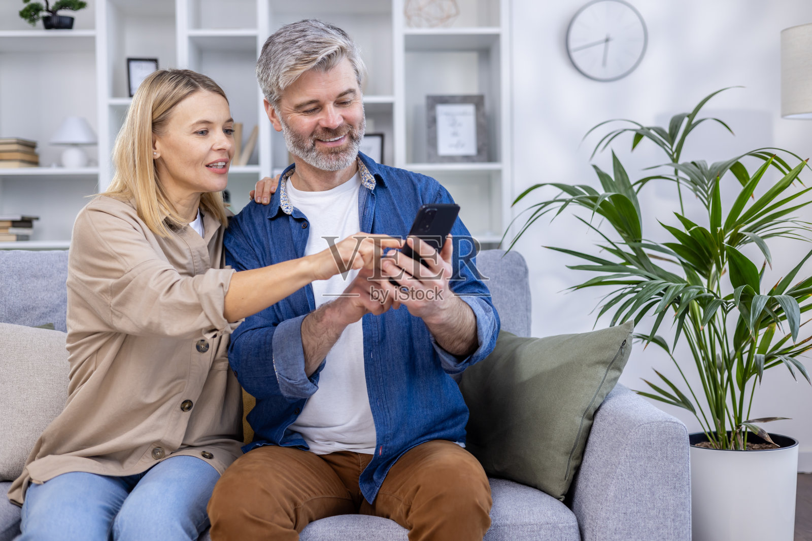 幸福的夫妇坐在沙发上看智能手机，微笑着在家里享受时光照片摄影图片