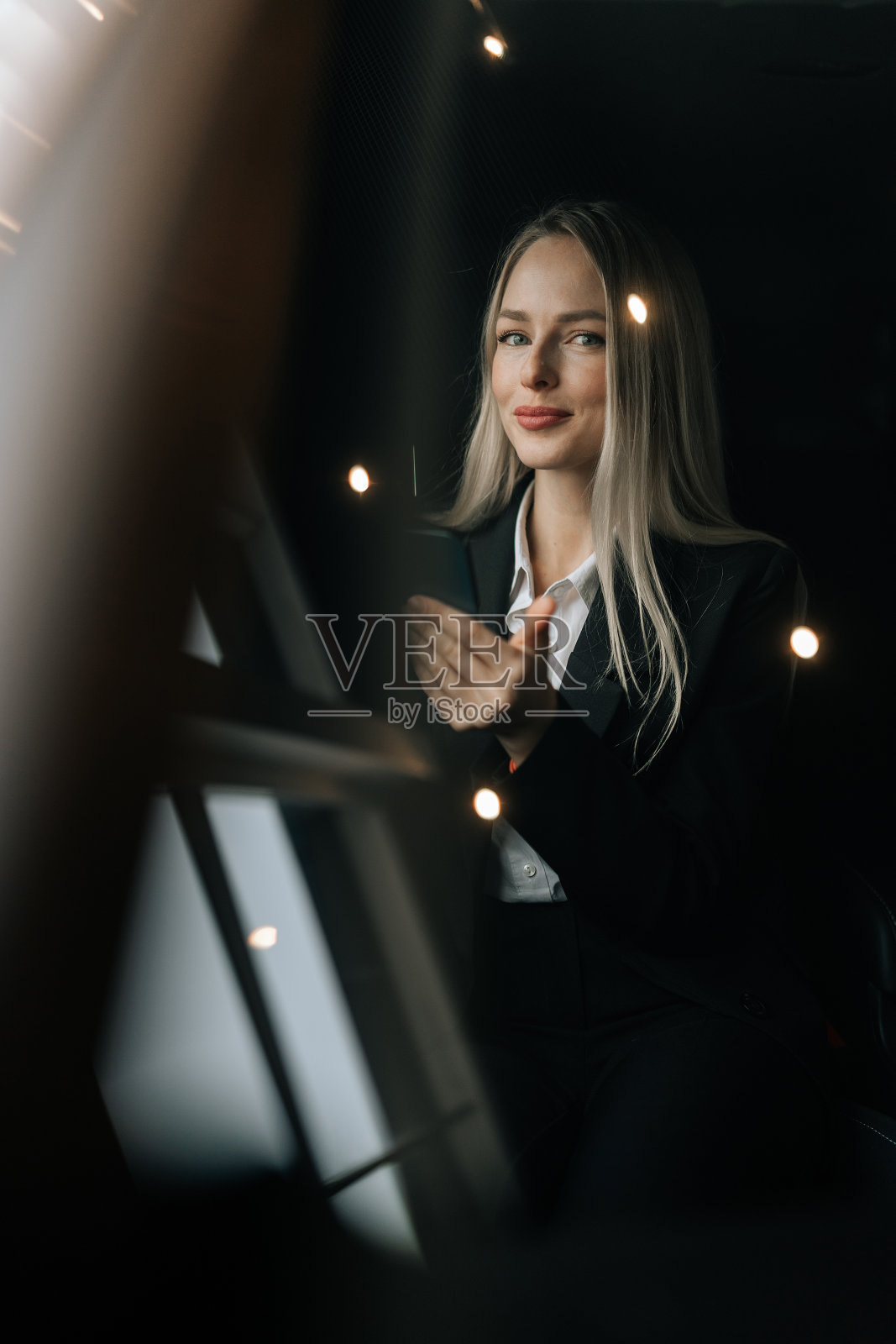 通过挡风玻璃的垂直照片，可以看到坐在汽车前座用智能手机看新闻的迷人女乘客。漂亮的年轻女子在浏览手机照片摄影图片