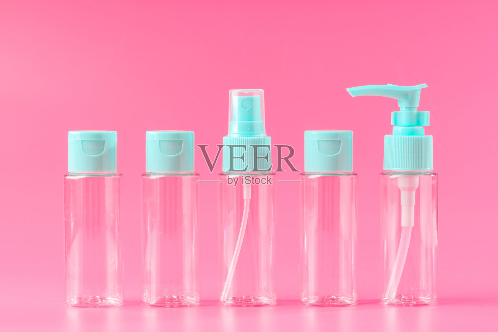 粉红色背景上有浅蓝色瓶盖的五个空旅行瓶照片摄影图片