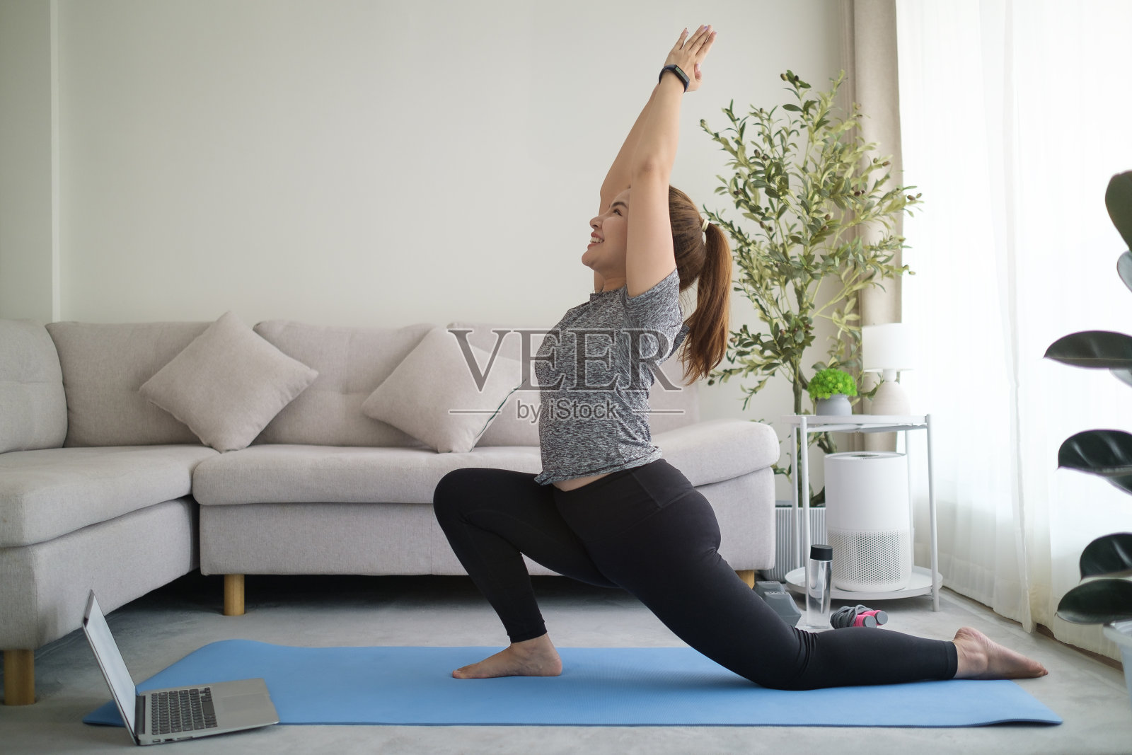 在明亮的客厅里，一名年轻女子正以战士的姿势站在垫子上做瑜伽。健康生活习惯概念照片摄影图片