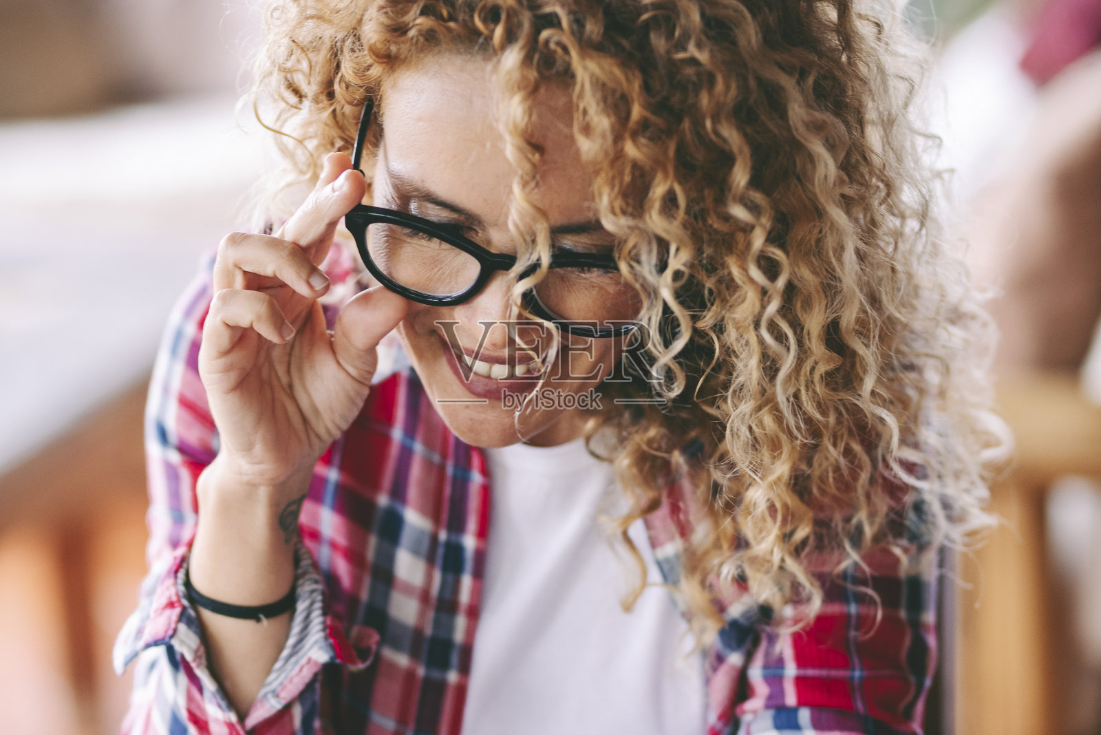 一个快乐的女人微笑着，开心地看着手机，独自坐在桌子旁。女性喜欢通过智能手机进行连接和现代通信。美女在线活动照片摄影图片