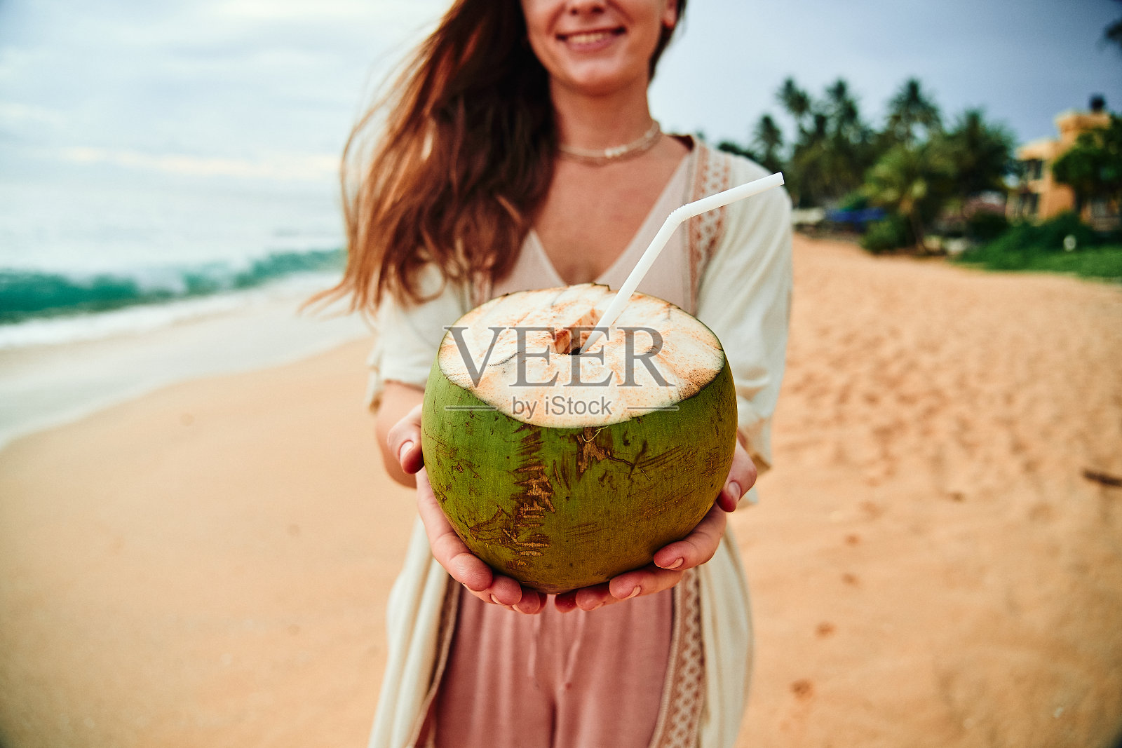 波西米亚女孩旅行者手里拿着一个热带绿色椰子和一根稻草在海边照片摄影图片