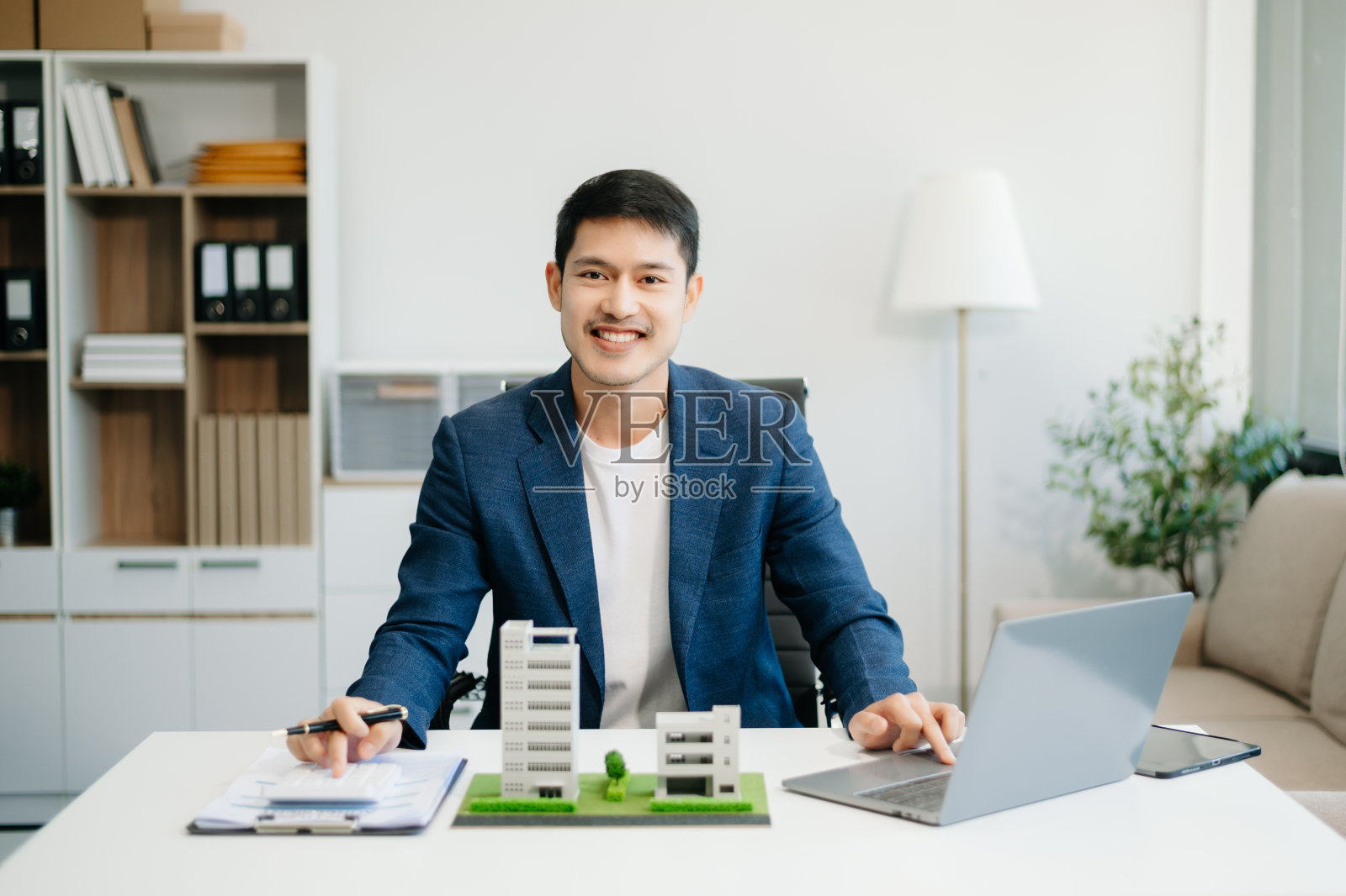 年轻的房地产经纪人在办公室和小房子的桌子上用笔记本电脑和平板电脑工作照片摄影图片