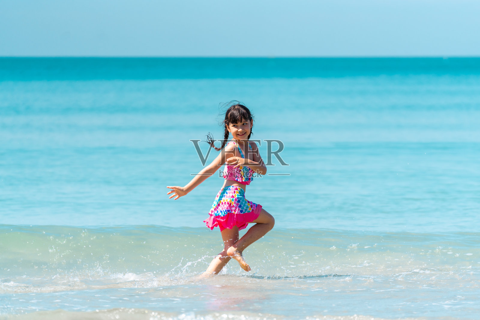 一个穿着泳装的小女孩，暑假在热带海滩上奔跑玩耍。照片摄影图片