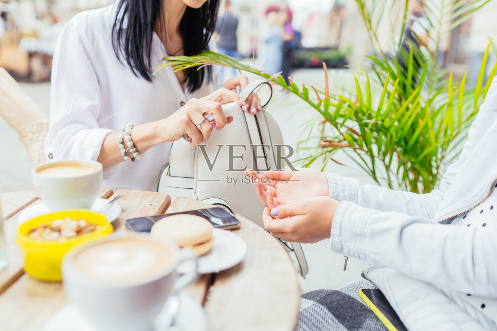 当她们在城市露天咖啡馆放松时，一名女性正在用抗菌消毒剂给她十几岁的女儿消毒。大流行概念后新的社会规则。照片摄影图片