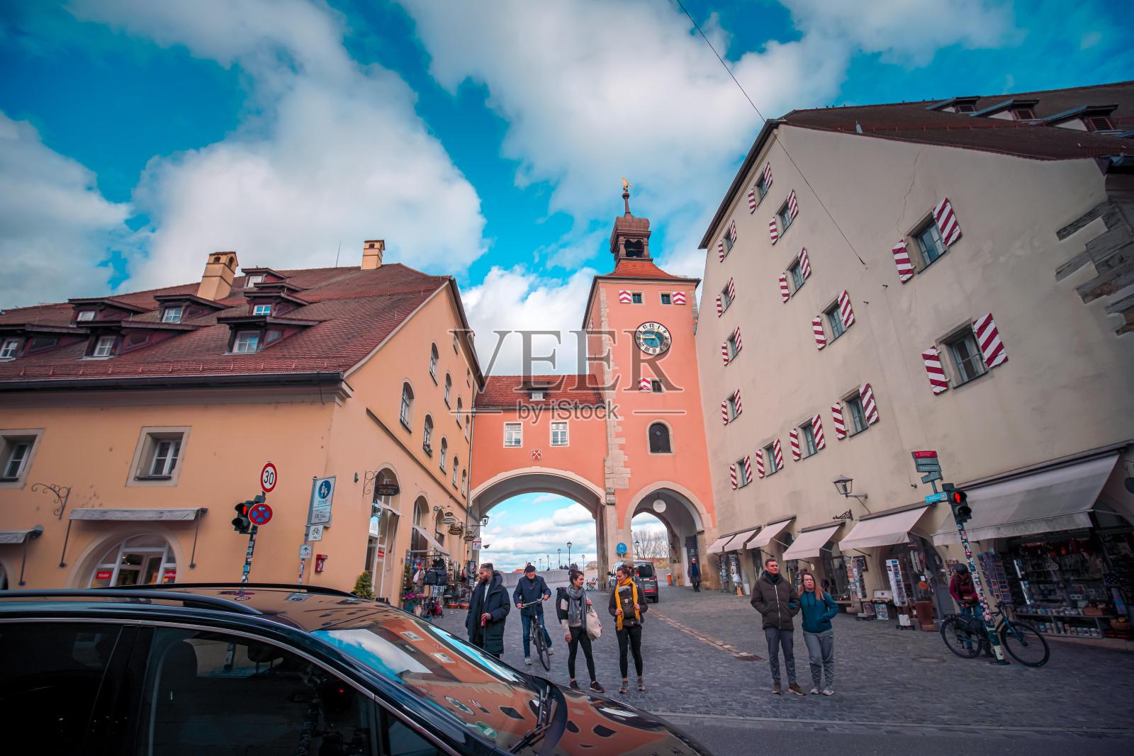 欧洲城市的街道，有历史建筑和钟楼。人们走在商店附近的鹅卵石街道上。一辆汽车停在图像的左侧。照片摄影图片