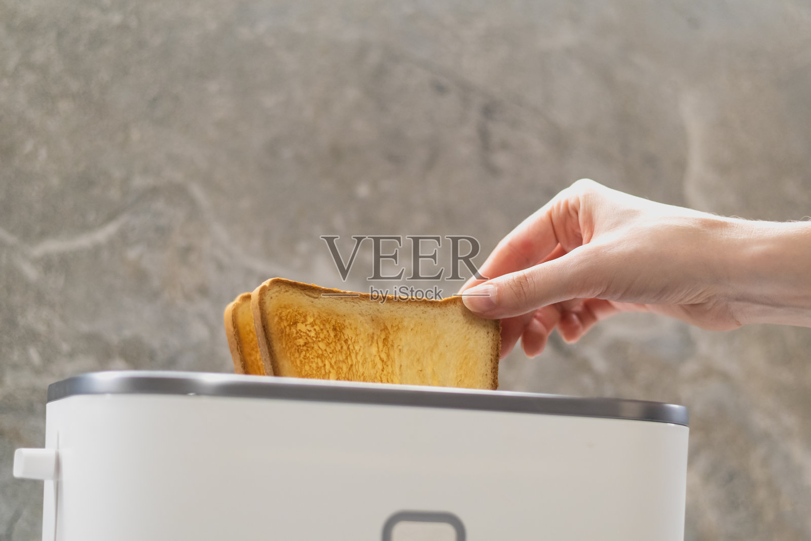 女人的手拿着从白色烤面包机里弹出的烤面包。近距离拍摄女人的手。关闭了。照片摄影图片