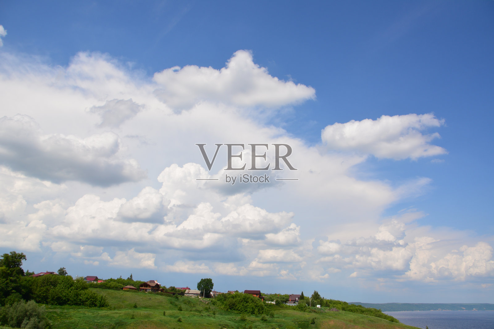 一片绿色的田野上有几座房子，一片水面上有天空中的云照片摄影图片