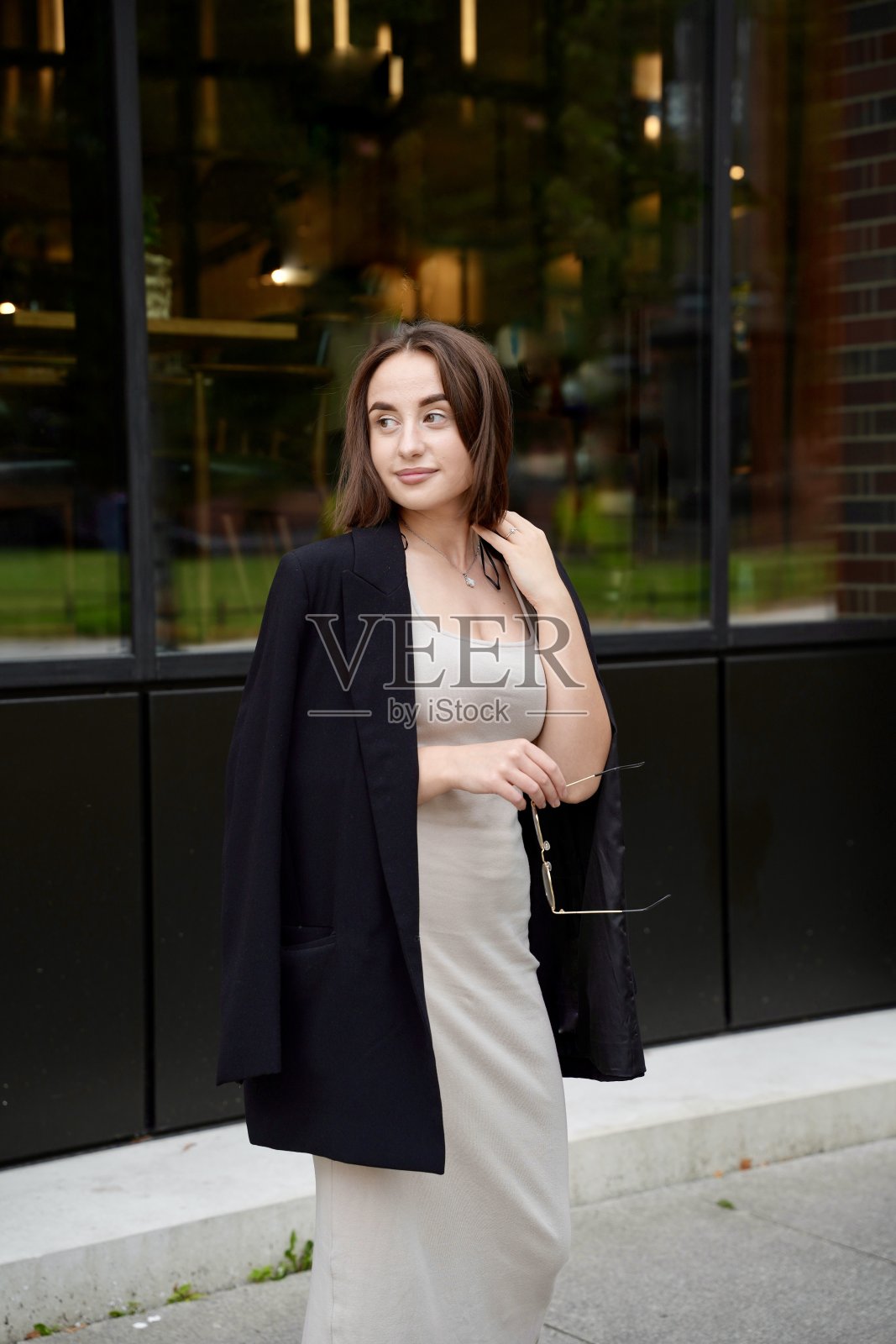 一个穿着夹克、剪着短发、手里拿着眼镜的商业女孩的肖像，背景是一栋建筑照片摄影图片