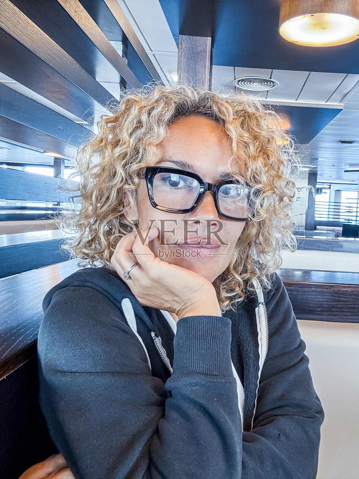 乘船旅行时坐在餐桌旁的金发美女经理。卷发戴黑眼镜的女人在旅行时使用笔记本电脑。数字游牧民的概念。照片摄影图片