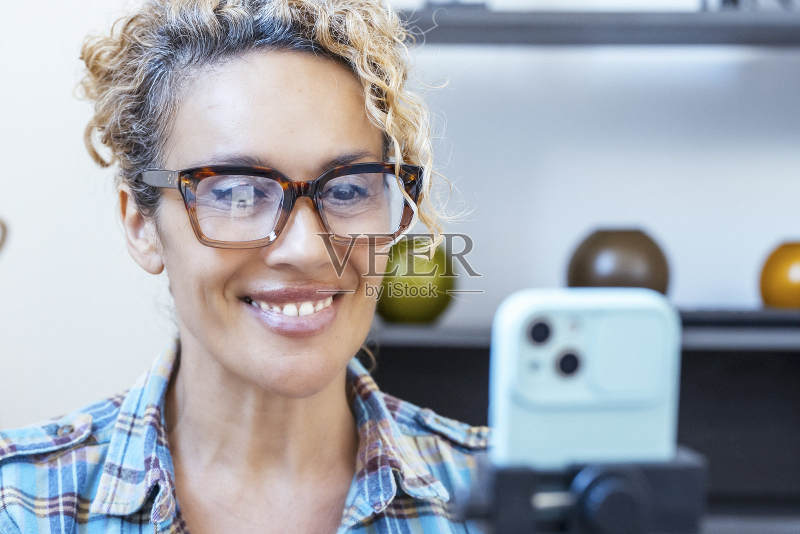 迷人的中年妇女在家里用手机拍摄视频。另一种自由职业者的生活方式和在家工作的概念。照片摄影图片