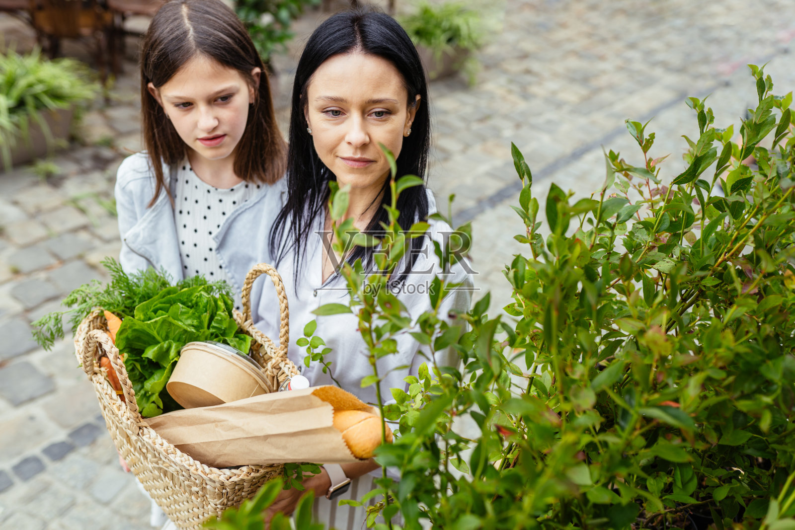 带着可爱的十几岁的女儿，带着草包在农贸市场购物的当代黑发女人，在街头农贸市场选择生态蓝莓。照片摄影图片