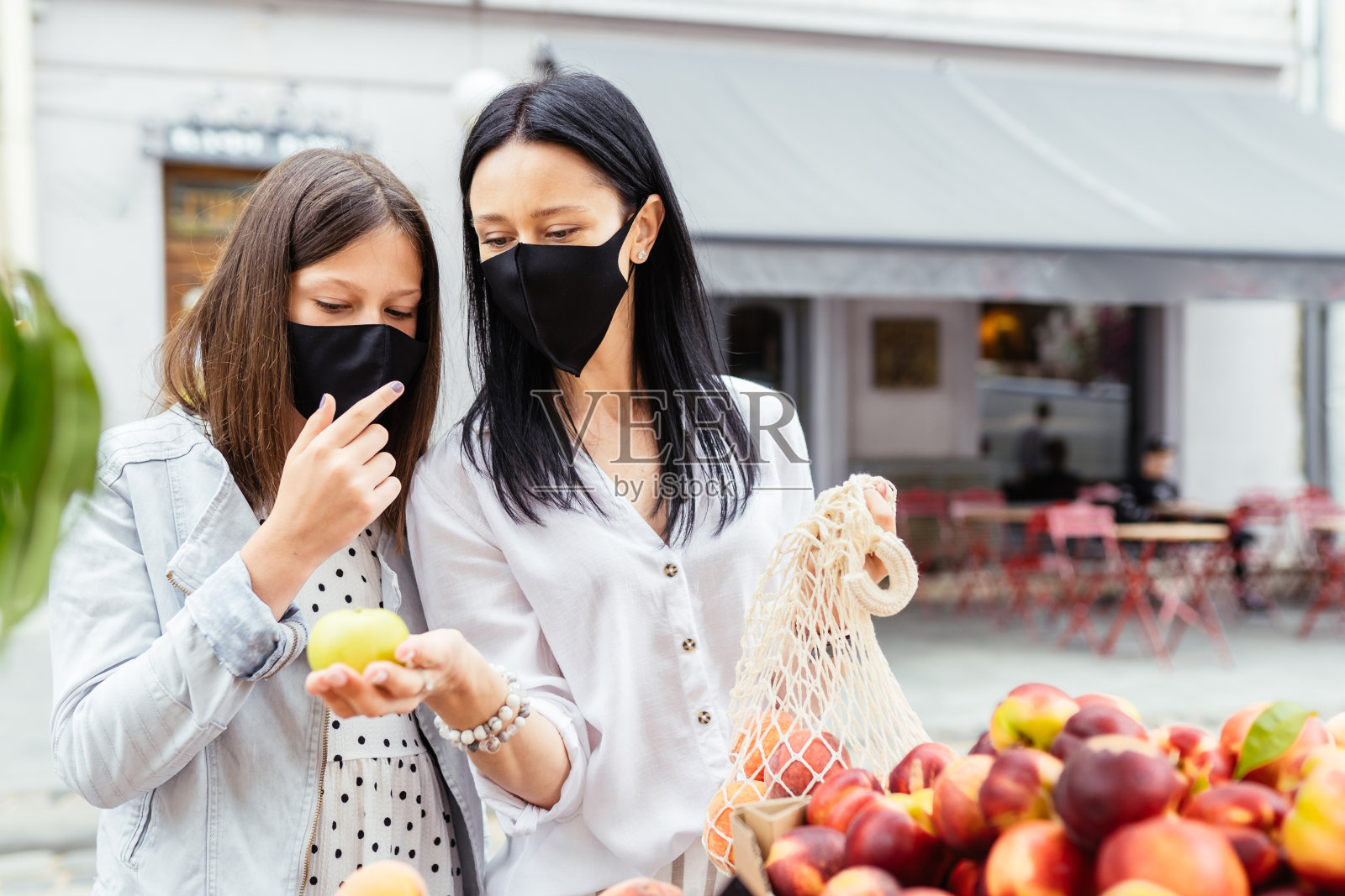 夏天，美女带着十几岁的女儿戴着防护口罩在农贸市场挑选有机桃子。可重复使用的环保购物袋。零废物概念。照片摄影图片