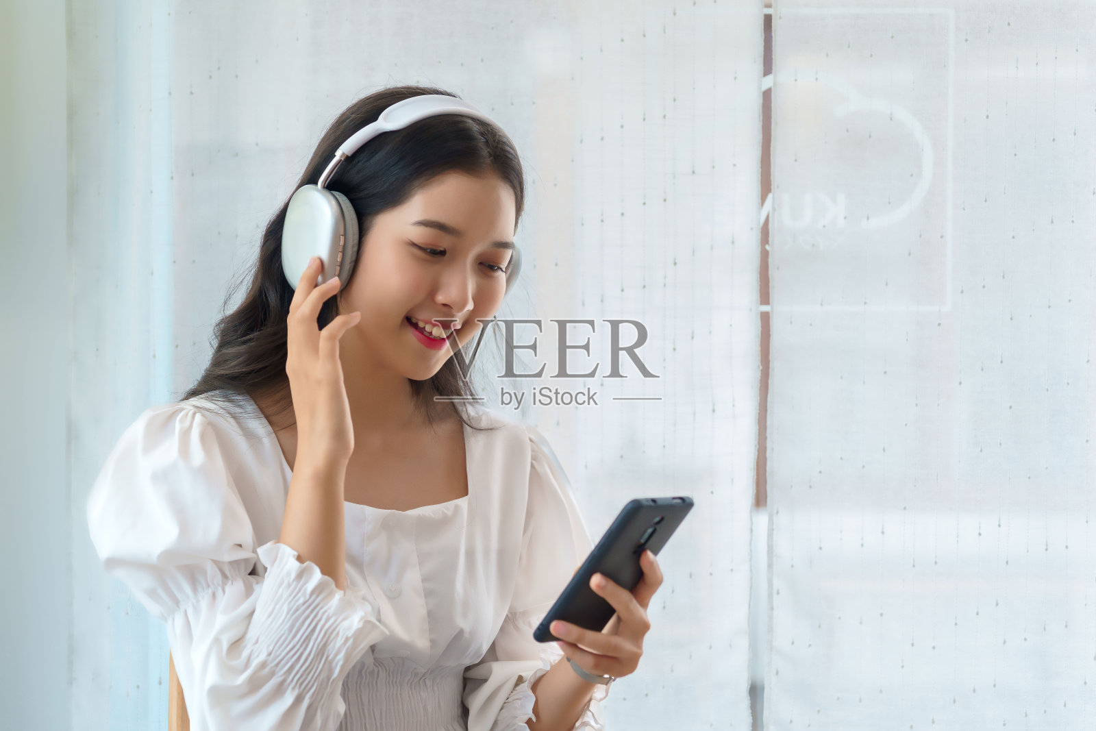 年轻的亚洲女商人在分析了投资策略和新创业项目的规划后，戴着耳机听音乐，在智能手机上刷社交媒体，在咖啡馆工作照片摄影图片