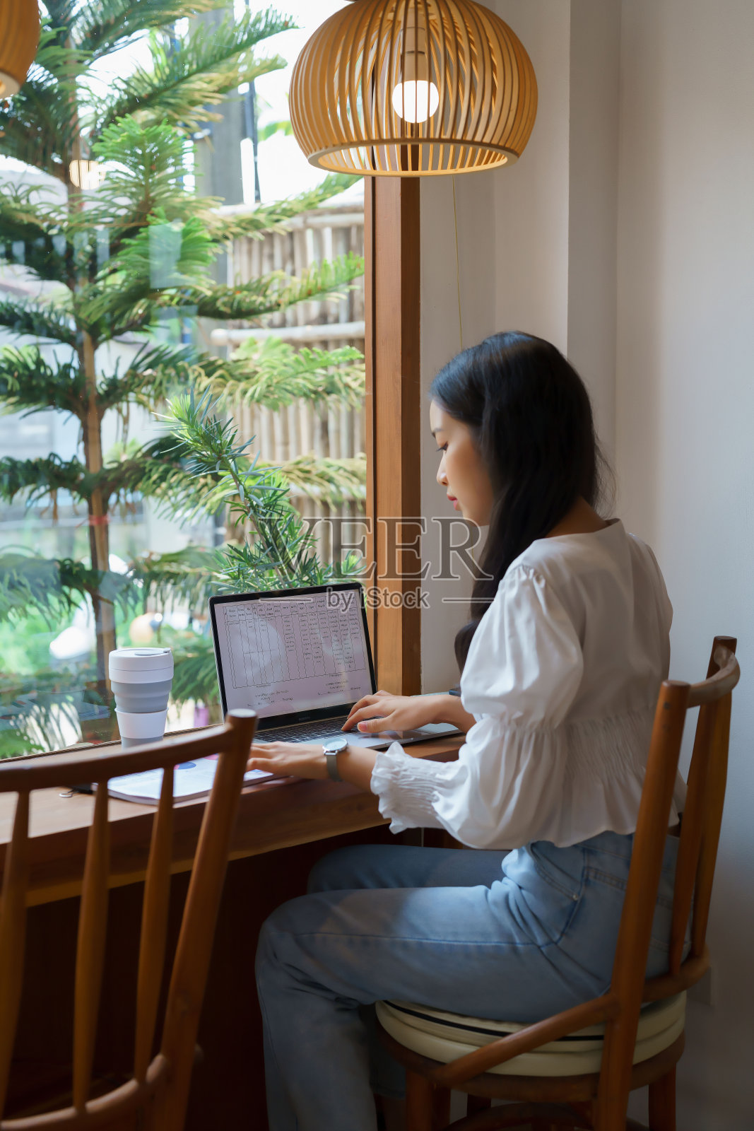年轻的亚洲女商人一边阅读文件上的商业营销数据，一边在笔记本电脑上输入图表信息，一边在咖啡馆工作，思考新的创业项目的投资和规划照片摄影图片