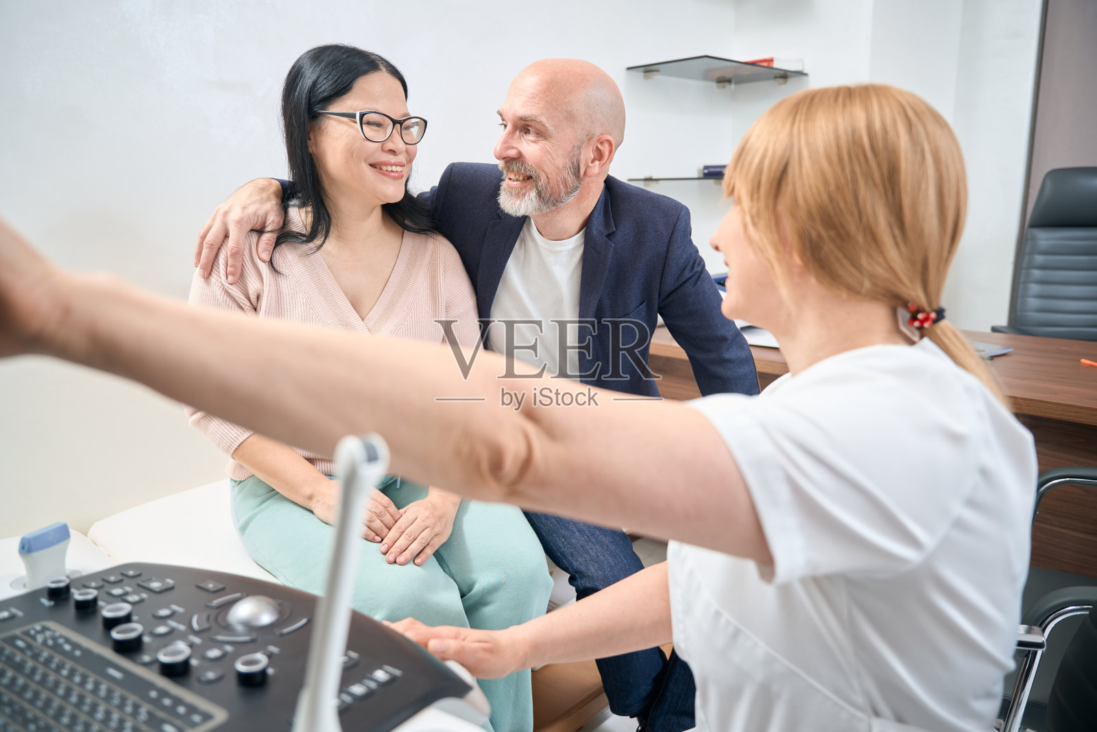 妇科超声医师向成年混血儿夫妇展示胎儿图像照片摄影图片