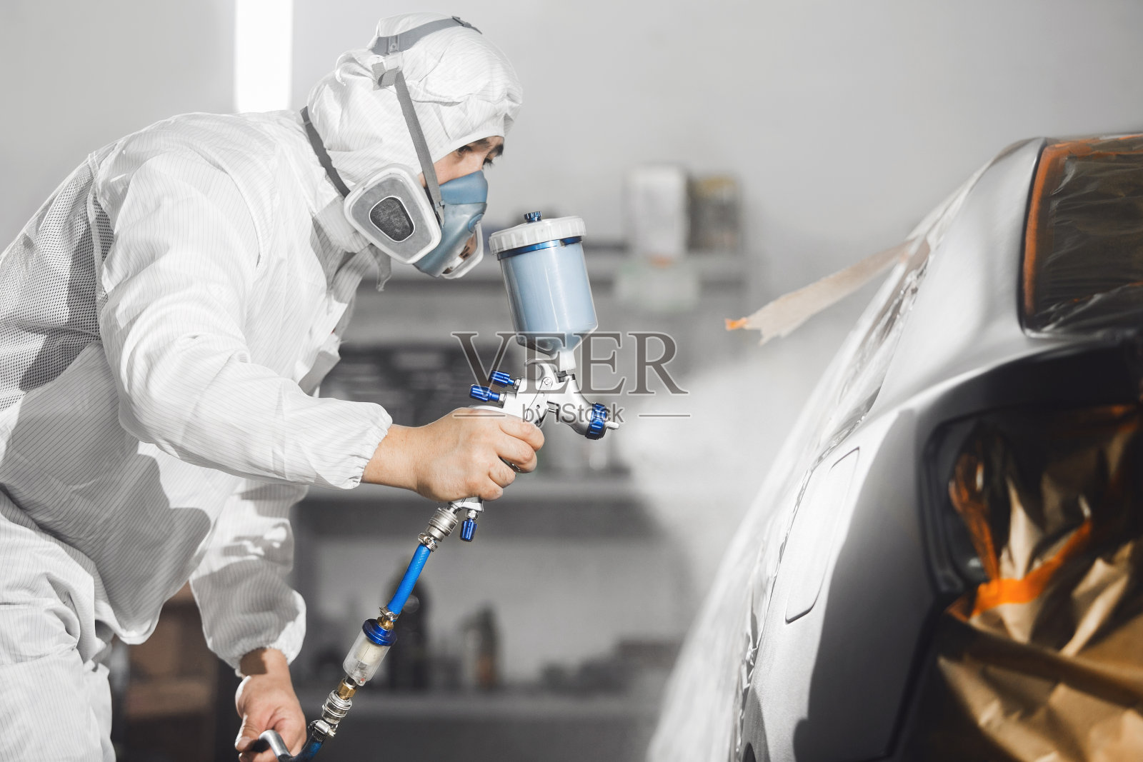 汽车修理工在喷漆室用喷枪对黑色车身进行喷漆。照片摄影图片