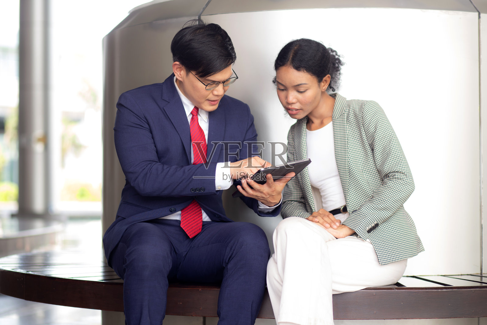 两个年轻的商人男女在正式的会议上讨论文件和使用平板电脑在现代办公室，商人计划与合作伙伴或咨询，商业和团队的概念。照片摄影图片