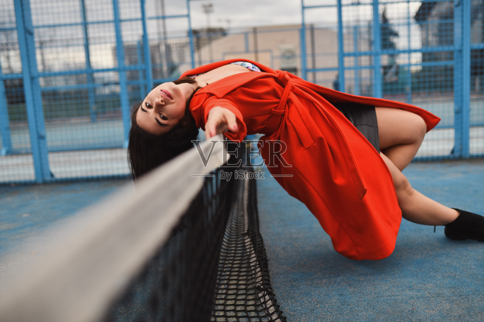 穿着红色外套的女士坐在网球网上的放松和诱惑照片摄影图片